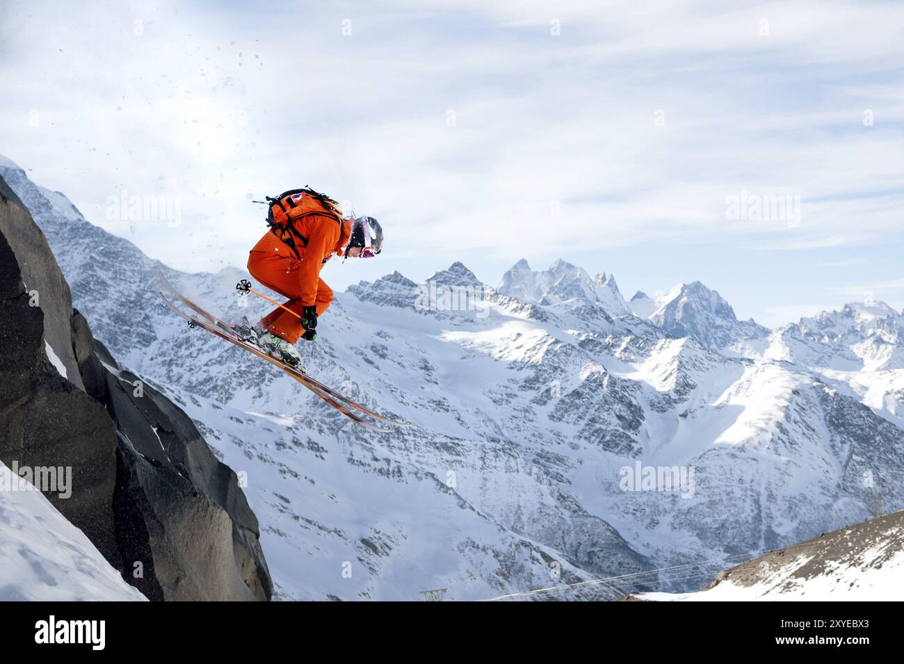 Uno sciatore professionista fa un salto da un'alta scogliera contro il cielo blu lasciando una scia di neve in montagna. Cresta caucasica nel Foto Stock