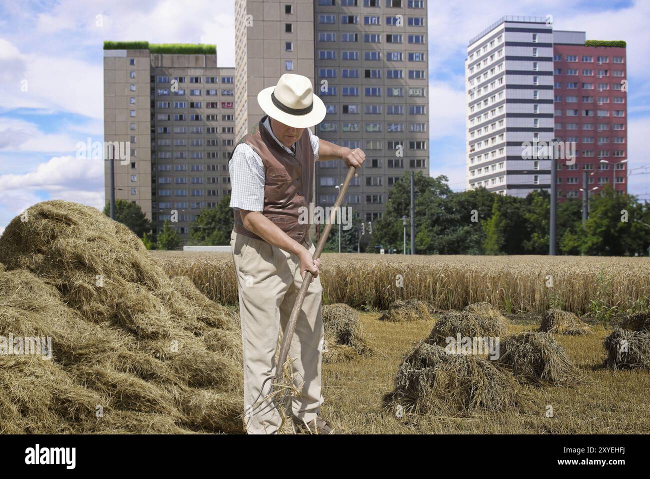 Contadino che gira fieno in una zona residenziale vicino alla città Foto Stock