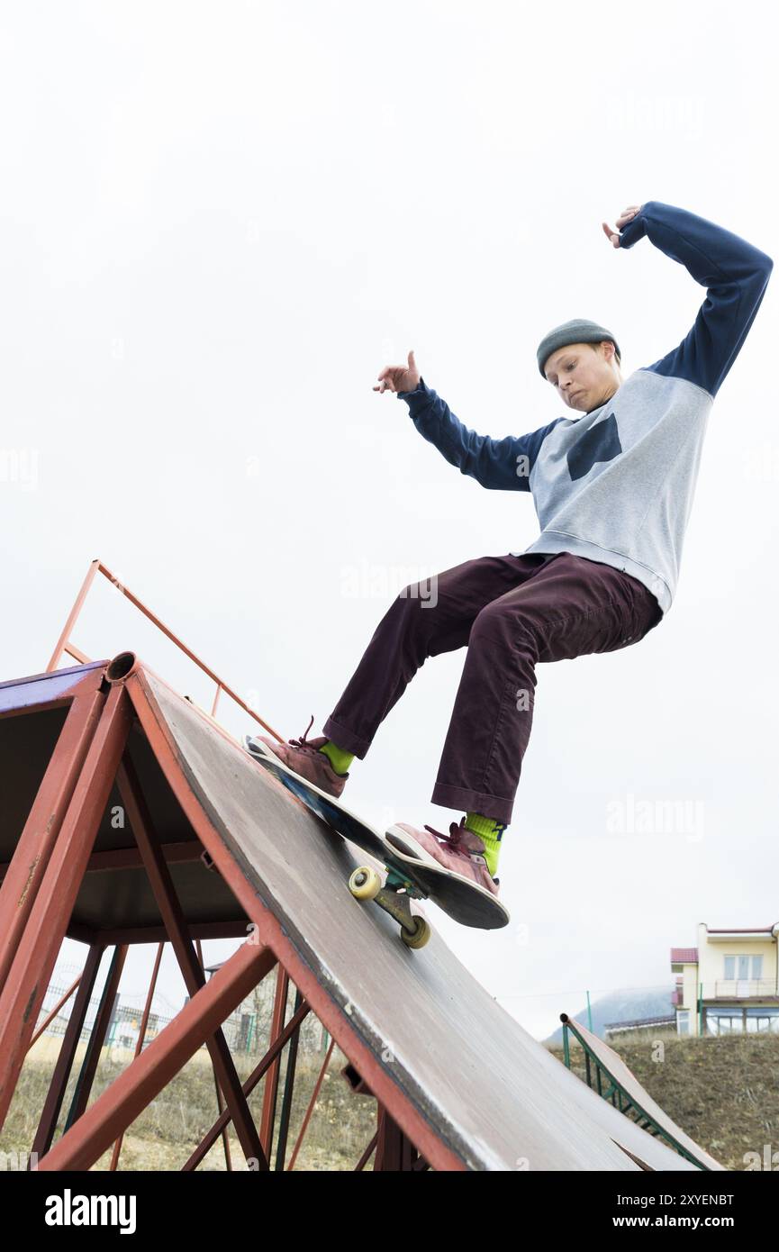 Skater adolescente in felpa con cappuccio e jeans scivola su una ringhiera su uno skateboard in uno skate Park, grandangolare Foto Stock