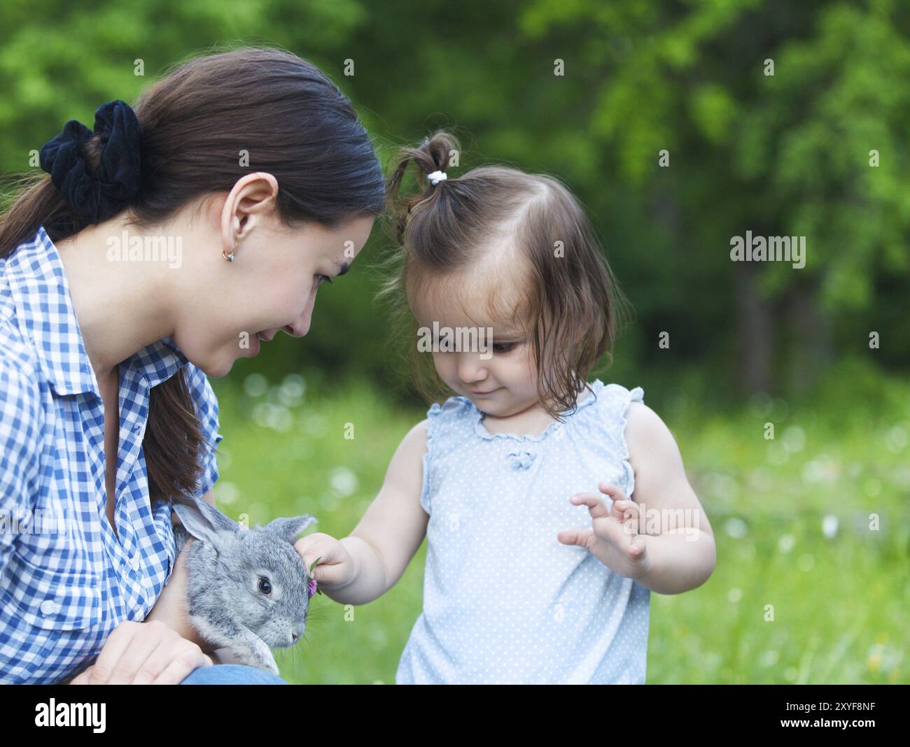 Carino bambina e sua madre abbracciando piccolo coniglio grigio. L'amicizia e il concetto di cura Foto Stock