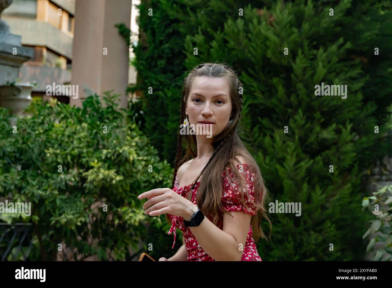 Una donna dai capelli rossi con un abito rosso floreale danzerà gioiosamente con il telefono in mano, catturando l'essenza di una giornata di sole guardando la fotocamera. Foto Stock