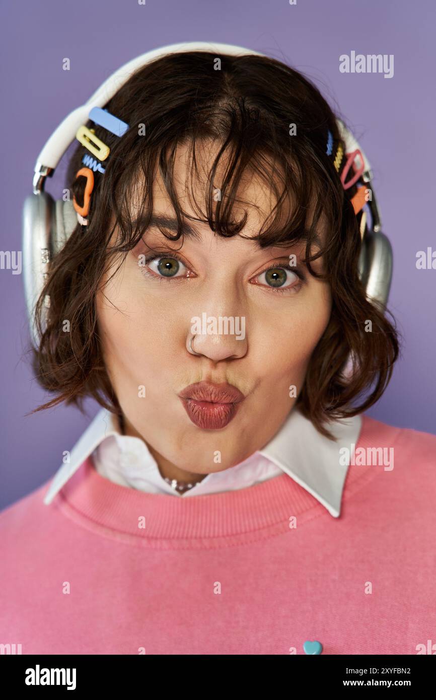 Una donna che indossa le cuffie e un maglione rosa crea un volto giocoso. Foto Stock