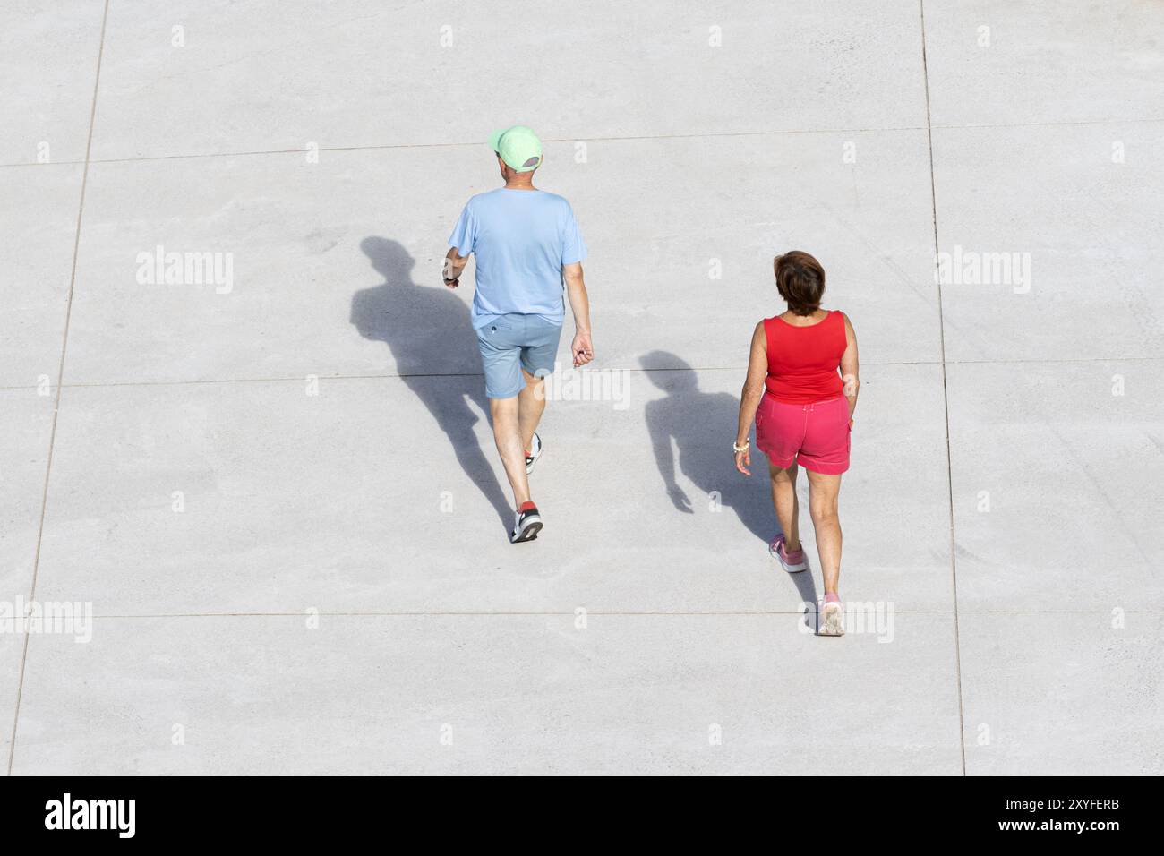 Uomo maturo e donna che camminano su un sentiero di cemento durante il giorno, uno in rosso e l'altro in blu, godendosi un momento informale insieme. Vista ad angolo alto Foto Stock Uomo maturo e donna che camminano su un sentiero di cemento durante il giorno, uno in rosso e l'altro in blu, godendosi un momento informale insieme. Vista ad angolo alto Foto Stock