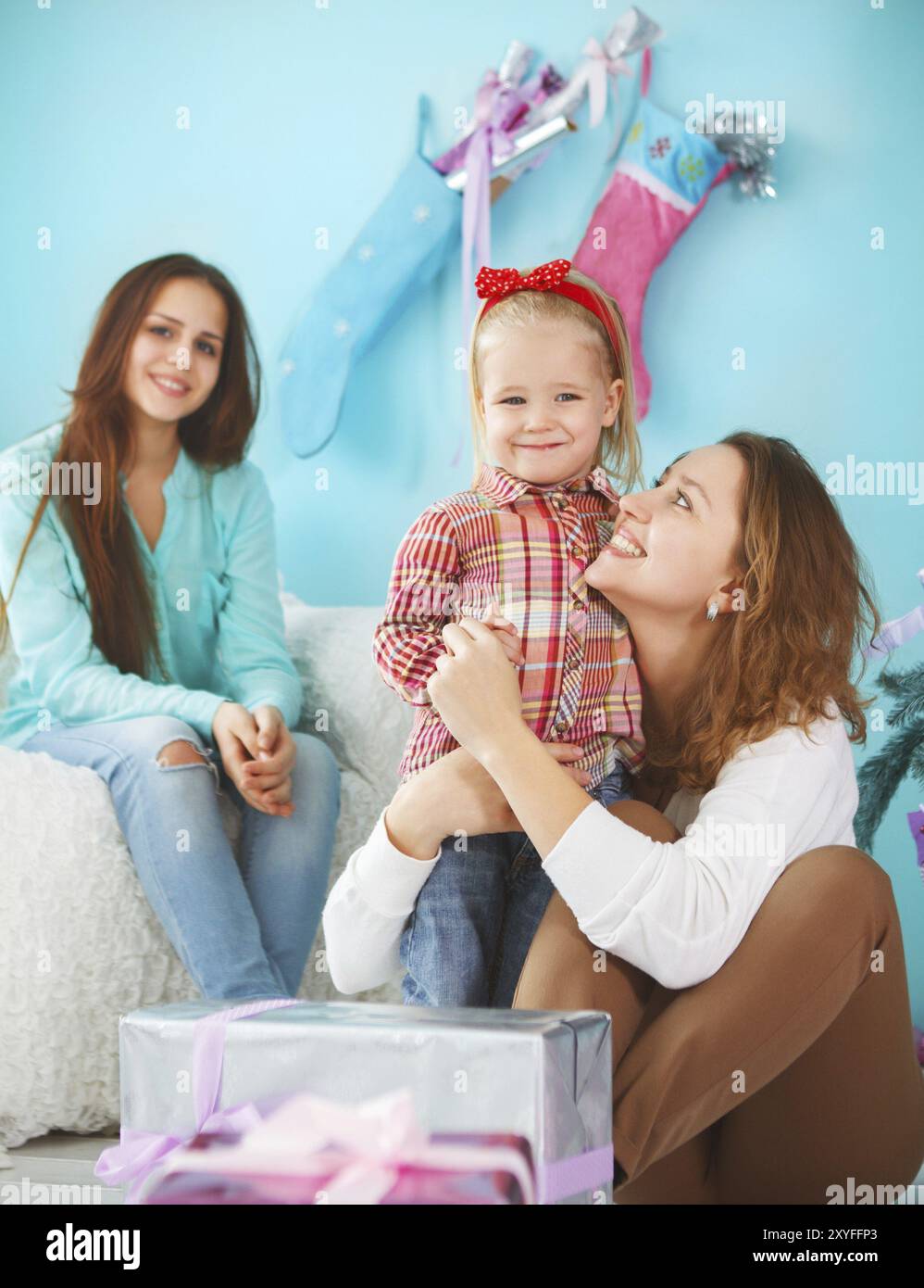 Ritratto di una madre con una bambina e una figlia adolescente che si avvicinano e si abbracciano a casa vicino all'albero di Natale e sono felici e gioiosi Foto Stock