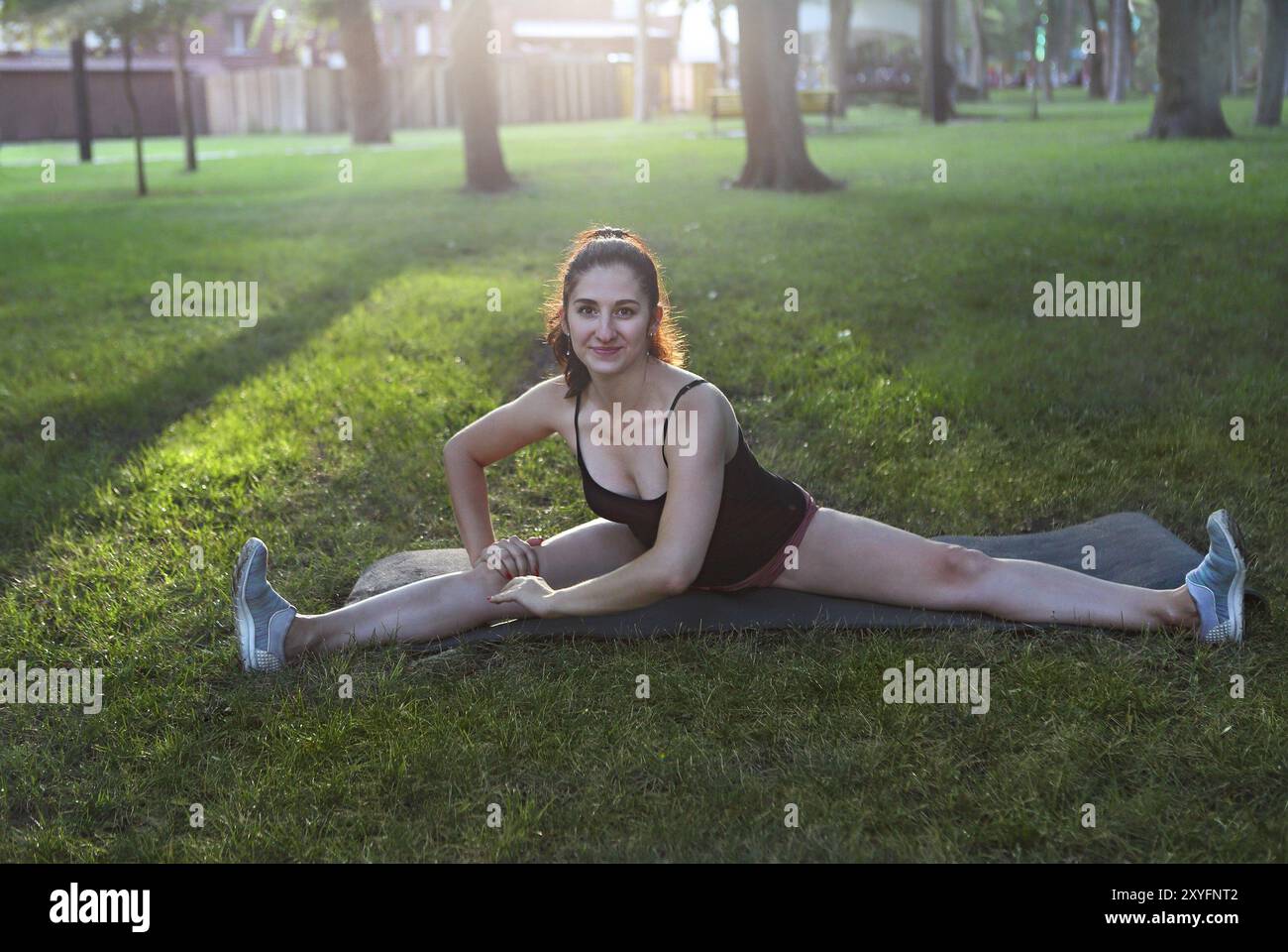Donna che si allunga in un esercizio all'aperto sorridente felice facendo stretching dopo la corsa. Splendido modello sportivo sorridente all'aperto al tramonto d'estate Foto Stock