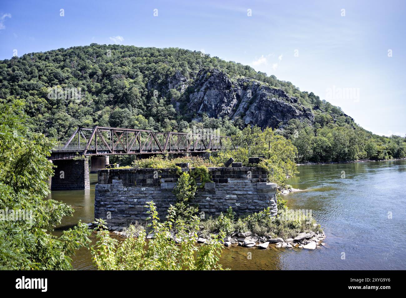 Harpers Ferry Railway Bridge Potomac River West Virginia // HARPERS FERRY, West Virginia - Vista dal Lower Town Harpers Ferry attraverso il fiume Potomac verso Maryland Heights, con lo storico ponte ferroviario e i resti dei piloni del Bollman Bridge in primo piano. Questa scena cattura l'importanza strategica di questo storico attraversamento del fiume e il suo ruolo nella storia dei trasporti americani. Foto Stock