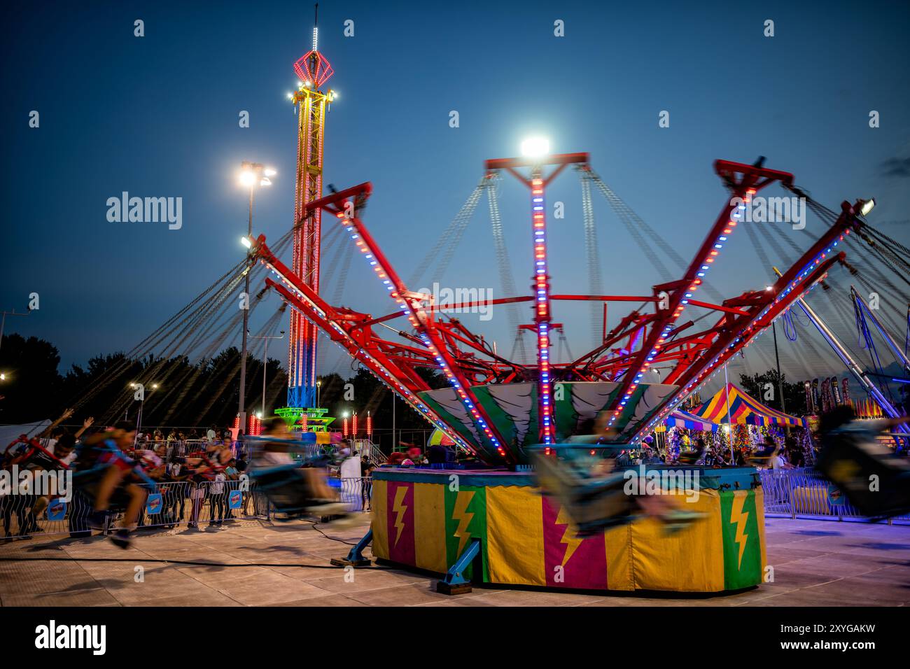 Altalena Fiera della Contea di Arlington Arlington Virginia | ARLINGTON, Virginia — Un'altalena colorata gira in movimento durante le ore serali alla Fiera della Contea di Arlington, che si tiene ogni agosto al Thomas Jefferson Community Center e Park ad Arlington, in Virginia. La fiera è gratuita e attira oltre 150.000 visitatori all'anno, rendendola uno dei più grandi eventi gratuiti della costa orientale. Fa risalire le sue origini a una modesta "Giornata del raccolto" nel 1977 organizzata da giardinieri della comunità e membri di 4-H — la prima edizione non aveva né luna park né giostre. L'attrazione illuminata che gira su un d Foto Stock