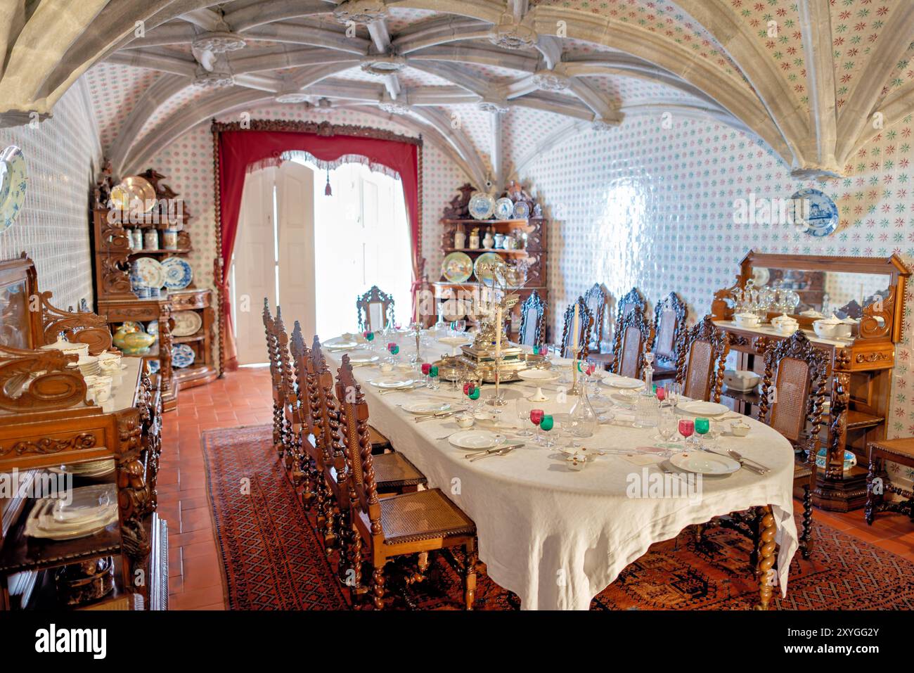 Pena Palace Dining Room Sintra Portugal // SINTRA, Portugal — la sala da pranzo del pena Palace, ex refettorio dei monaci geronimiti, convertita da re Ferdinando II nella sala da pranzo privata della famiglia reale portoghese. La sala presenta archi a volta a costola manuelina del XVI secolo ed è rivestita con piastrelle del XIX secolo di Fábrica Roseira. I mobili in quercia furono commissionati da re Ferdinando II nel 1866 a Casa Barbosa e Costa. Palazzo pena, patrimonio dell'umanità dell'UNESCO, rappresenta uno dei più bei esempi di architettura romantica del XIX secolo in Europa. Il palazzo Combine ha ottenuto Foto Stock