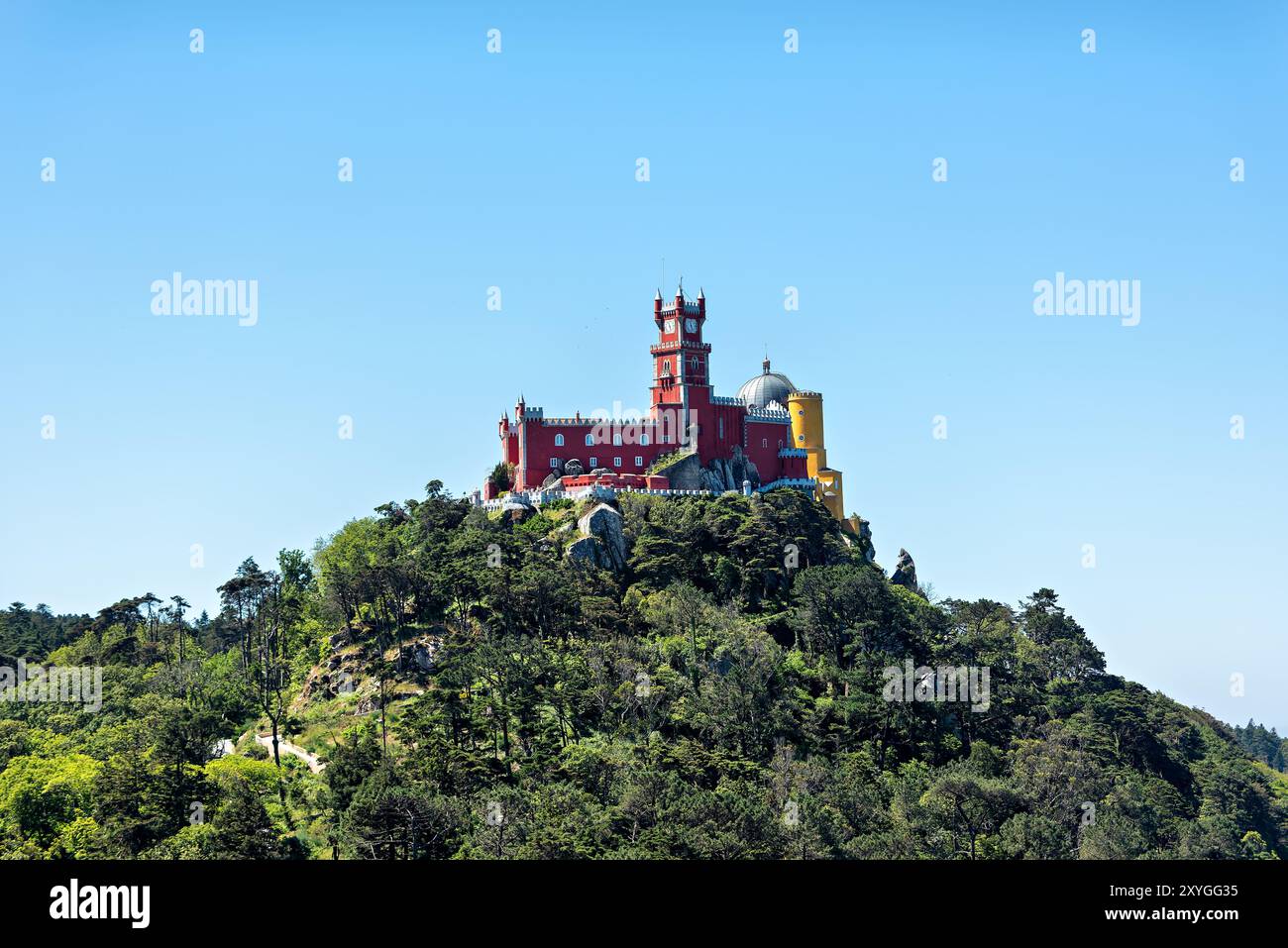 SINTRA, Portogallo - Palácio da pena, arroccato sulla cima di una collina dei Monti Sintra, visto da lontano. La colorata ed eclettica architettura di questo castello romanticista del XIX secolo si distingue drammaticamente contro il lussureggiante paesaggio verde, incarnando il fascino fiabesco per cui Sintra è famosa. Foto Stock