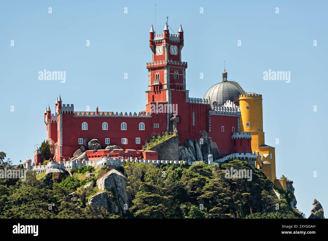 Palácio da pena Sintra Portogallo // SINTRA, Portogallo - Palácio da pena sorge in cima a una collina dei Monti Sintra. Il castello romanticista del XIX secolo presenta un'architettura colorata ed eclettica che contrasta con il lussureggiante paesaggio verde circostante. Costruito come residenza estiva per i reali portoghesi, il palazzo combina vari stili architettonici tra cui elementi gotici, rinascimentali, moreschi e manuelini. La struttura fu commissionata da re Ferdinando II e completata negli anni '1850 Oggi, il Palácio da pena funge da museo ed è riconosciuto come patrimonio dell'umanità dell'UNESCO come parte della rete culturale Foto Stock