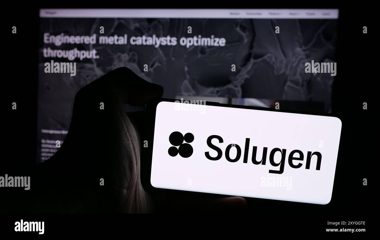 Persona che detiene un cellulare con il logo della società di produzione chimica statunitense Solugen Inc. Di fronte alla pagina Web aziendale. Mettere a fuoco il display del telefono. Foto Stock