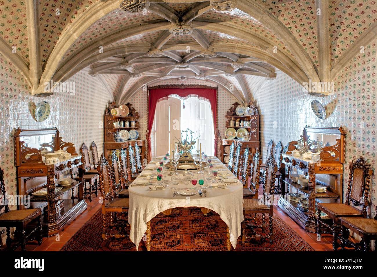 Pena Palace Dining Room Sintra Portugal // SINTRA, Portugal — la sala da pranzo del pena Palace, ex refettorio dei monaci geronimiti, convertita da re Ferdinando II nella sala da pranzo privata della famiglia reale portoghese. La sala presenta archi a volta a costola manuelina del XVI secolo ed è rivestita con piastrelle del XIX secolo di Fábrica Roseira. I mobili in quercia furono commissionati da re Ferdinando II nel 1866 a Casa Barbosa e Costa. Palazzo pena, patrimonio dell'umanità dell'UNESCO, rappresenta uno dei più bei esempi di architettura romantica del XIX secolo in Europa. Il palazzo Combine ha ottenuto Foto Stock