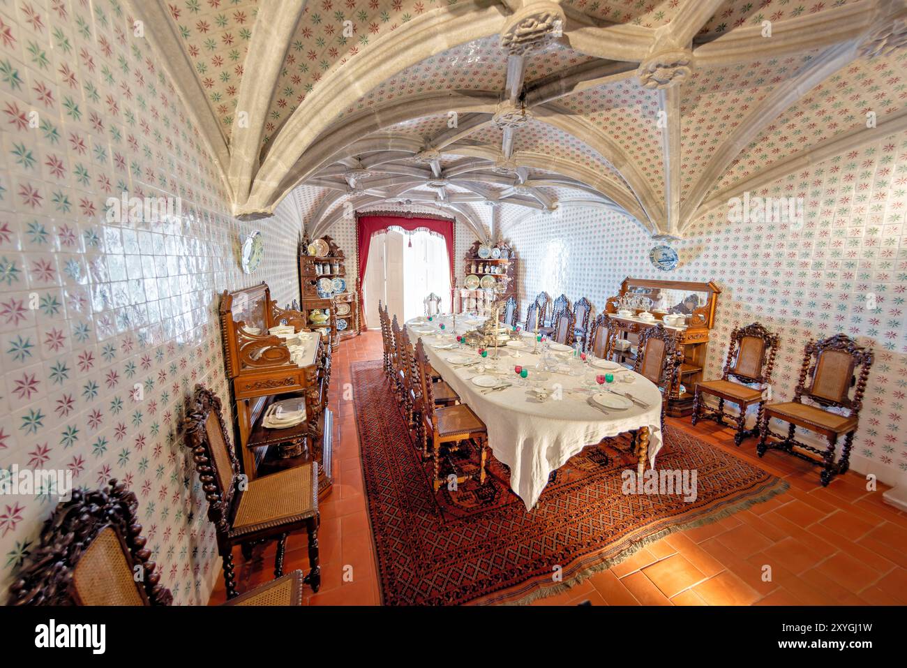 Pena Palace Dining Room Sintra Portugal // SINTRA, Portugal — la sala da pranzo del pena Palace, ex refettorio dei monaci geronimiti, convertita da re Ferdinando II nella sala da pranzo privata della famiglia reale portoghese. La sala presenta archi a volta a costola manuelina del XVI secolo ed è rivestita con piastrelle del XIX secolo di Fábrica Roseira. I mobili in quercia furono commissionati da re Ferdinando II nel 1866 a Casa Barbosa e Costa. Palazzo pena, patrimonio dell'umanità dell'UNESCO, rappresenta uno dei più bei esempi di architettura romantica del XIX secolo in Europa. Il palazzo Combine ha ottenuto Foto Stock