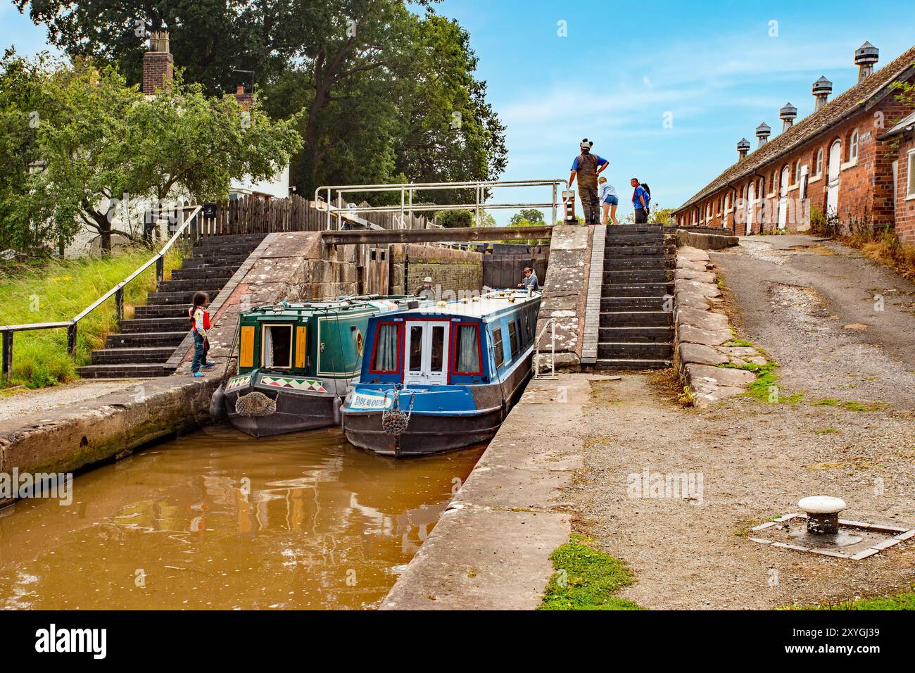 Le barche a remi passano attraverso le doppie chiuse a doppia scala sul canale Shropshire Union a Bunbury Cheshire con vista delle scuderie storiche Foto Stock