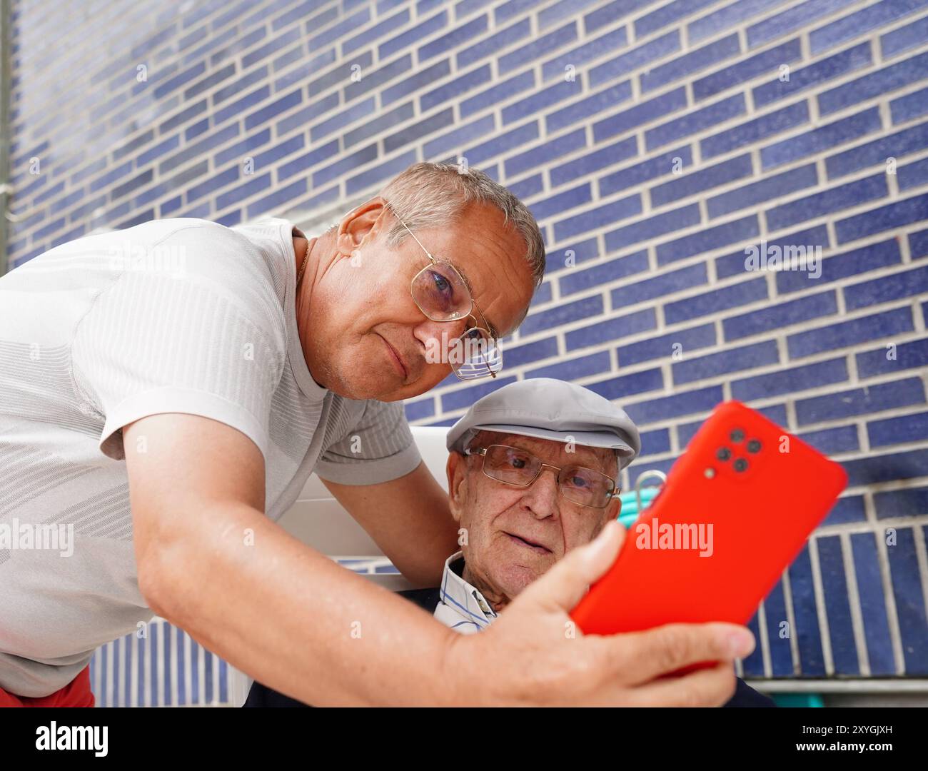 Padre e figlio guardano un video con il loro cellulare in terrazza. Gli uomini di famiglia Foto Stock