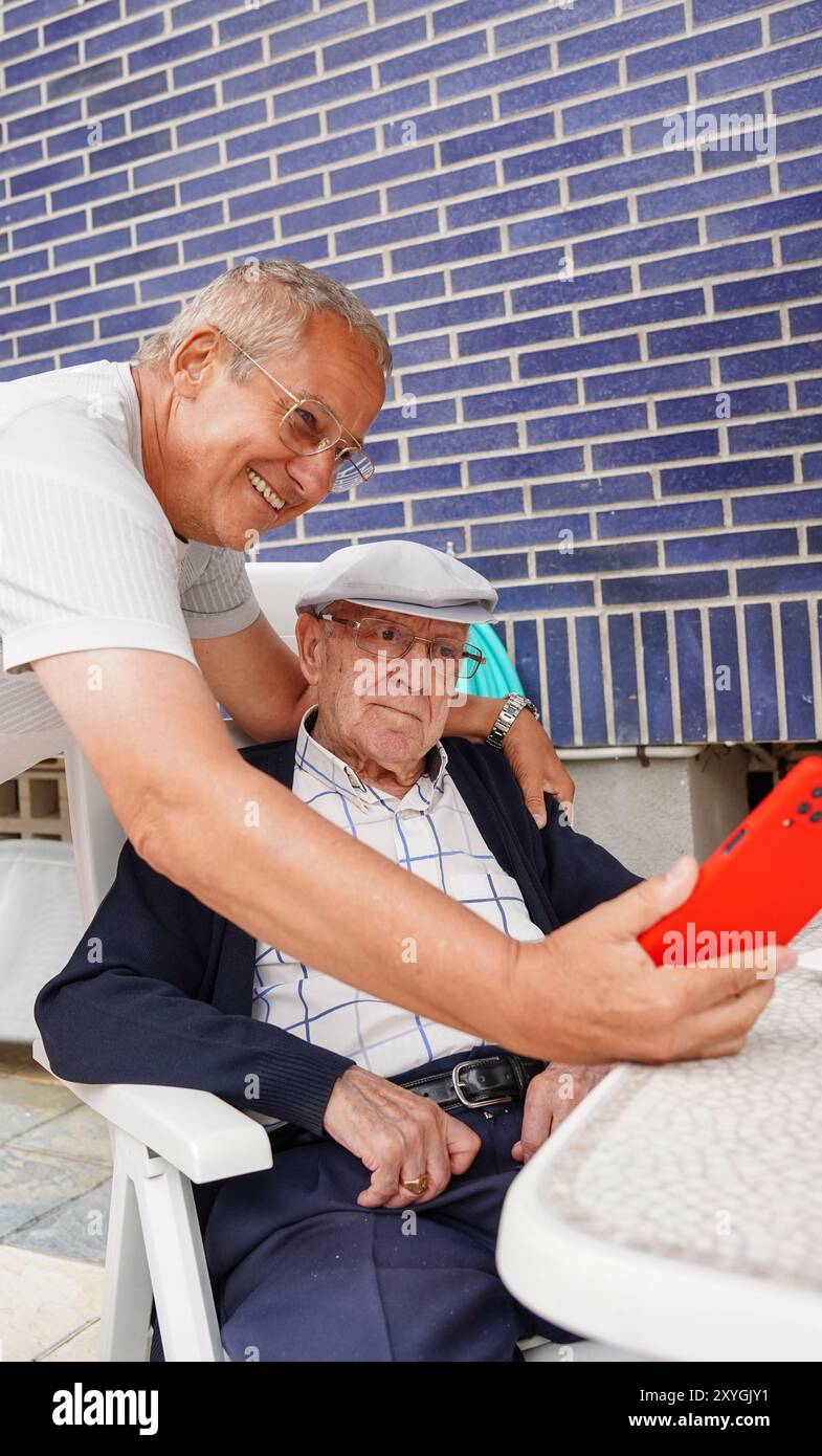 Padre e figlio guardano un video con il loro cellulare in terrazza. Uomini di famiglia Foto Stock