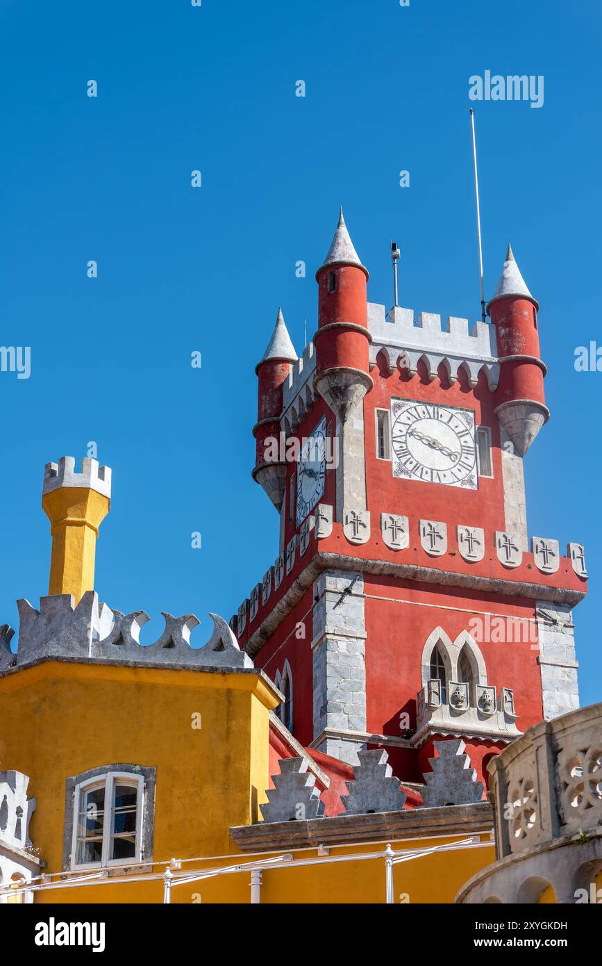 Torre dell'Orologio del Palazzo da pena Sintra Portogallo // SINTRA, Portogallo - la torretta dell'orologio rossa ornata del Palácio da pena si erge contro il cielo, mostrando i colori vivaci e l'eclettica architettura romanticista di questa residenza reale del XIX secolo. Questa caratteristica distintiva incarna il fascino fiabesco che rende il Palácio da pena un punto di riferimento imperdibile a Sintra. Foto Stock