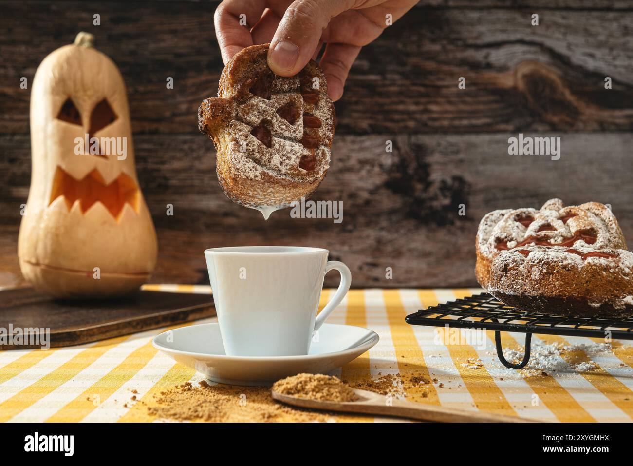 Un uomo irriconoscibile che prende un biscotto a forma di zucca e lo immerge nel latte, sullo sfondo una zucca di Halloween, in stile Halloween, il giorno dei morti. Foto Stock