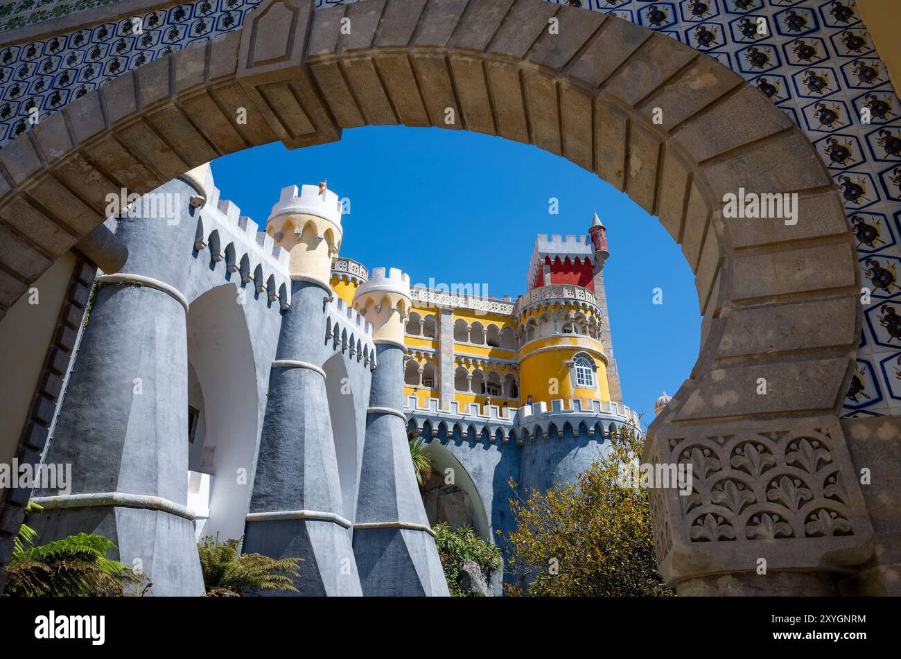 Architettura esterna del Palácio da pena Sintra Portogallo // SINTRA, Portogallo - l'architettura esterna vibrante ed eclettica del Palácio da pena, che mostra la sua miscela di stili romanticisti, moreschi e neo-manuelini. Costruito nel XIX secolo come residenza estiva per la famiglia reale portoghese, il palazzo fu commissionato da re Ferdinando II e completato nel 1854. Le facciate colorate, i dettagli ornati e gli elementi stravaganti incarnano l'architettura romantica e la visione di re Ferdinando II di un castello da favola. Situato in cima ai Monti Sintra, il palazzo fa parte del paesaggio culturale di Sintra, de Foto Stock