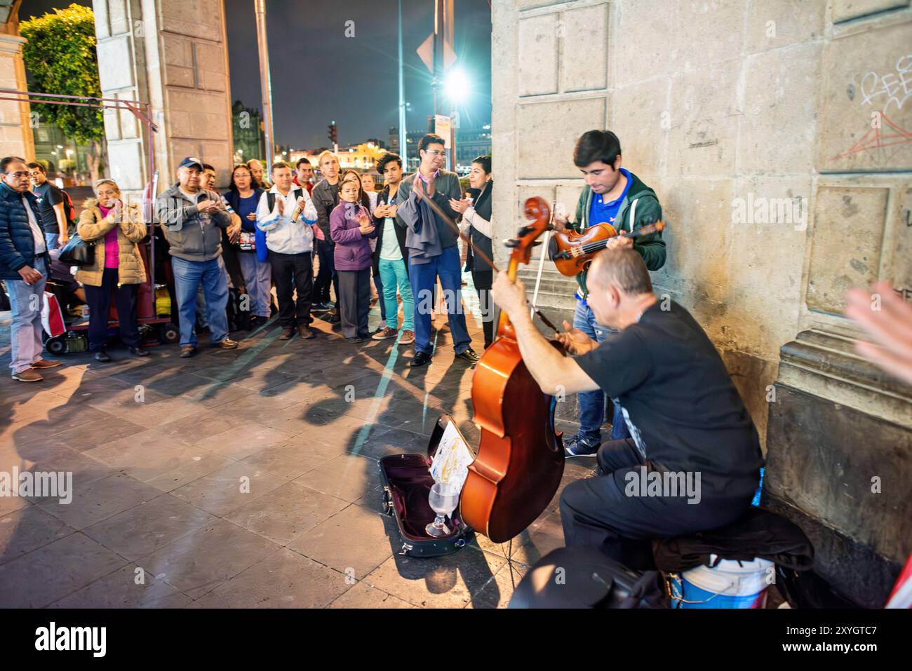 CITTÀ DEL MESSICO, Messico: Due musicisti di strada, un violinista e un violoncellista, si esibiscono di notte vicino al Zócalo, attirando una folla affascinata con la loro musica classica. Questo concerto improvvisato mette in mostra la vivace cultura di strada e la vita notturna del centro storico di città del Messico. Foto Stock