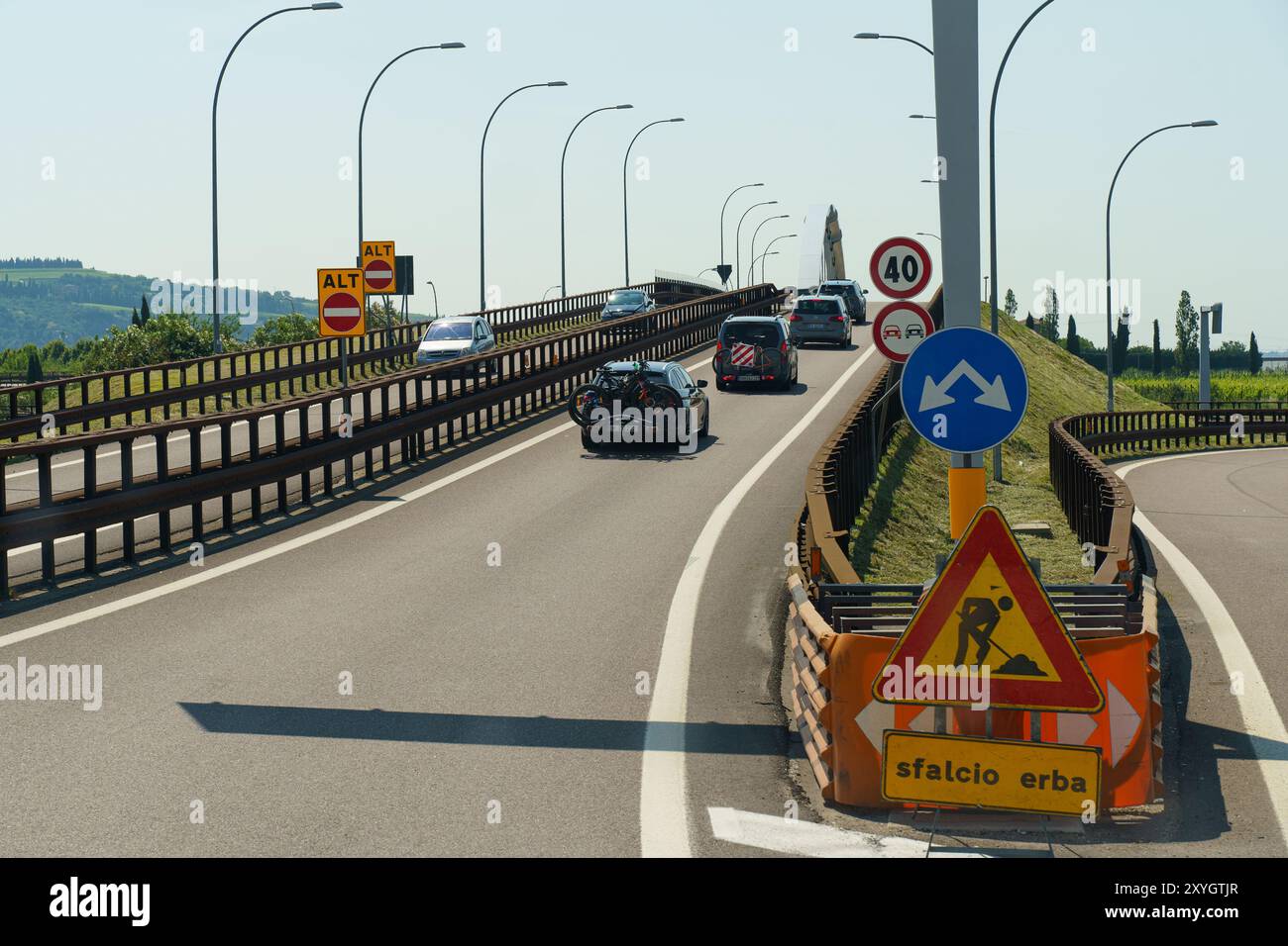 Progni, Italia - 8 giugno 2023: Le auto attraversano una tortuosa autostrada tra segnali di costruzione e segnali direzionali, incorniciata da rigogliose colline verdi nel bac Foto Stock
