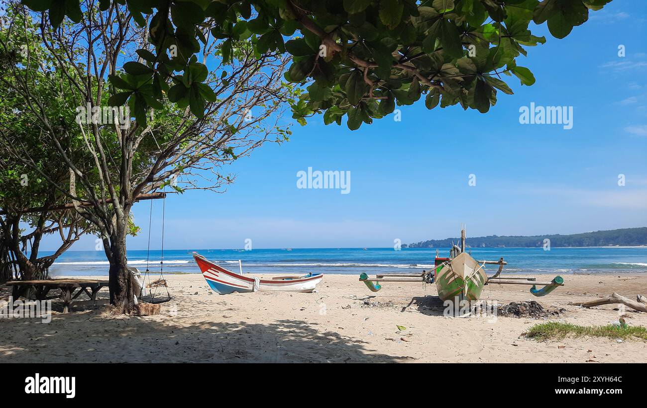 due barche da pesca su una spiaggia di sabbia bianca con alcuni alberi in una giornata di sole con cielo azzurro. concetto di immagine della destinazione di viaggio tropicale. Foto Stock