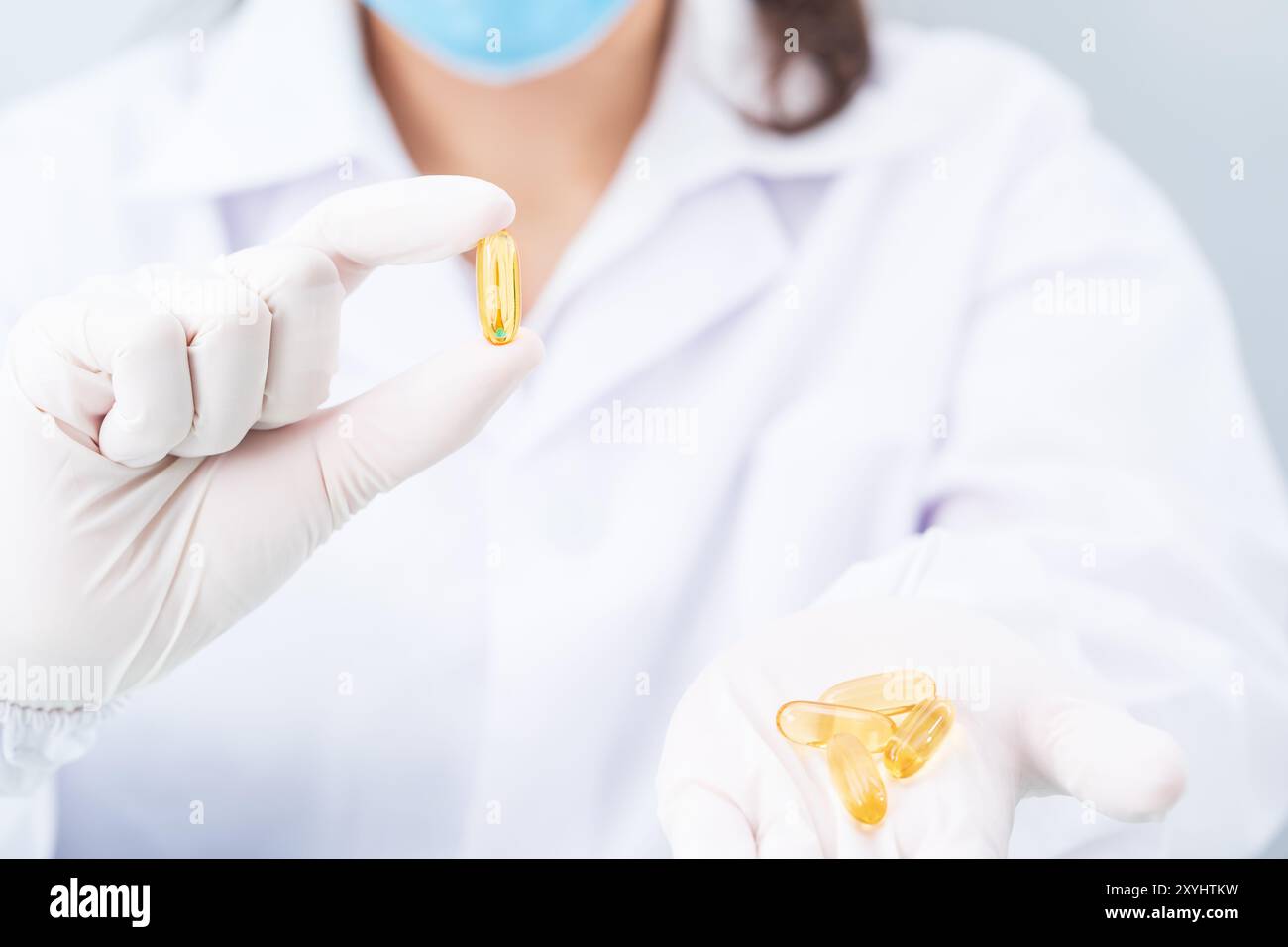 Primo piano mani biologo mettere in guanti in lattice di nitrile che tengono la capsula Omega 3 in camice da laboratorio indossando guanti in nitrile, facendo esperimenti in laboratorio Foto Stock