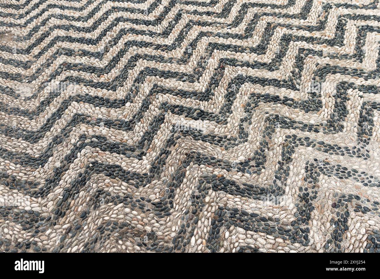 Pavimentazione stradale in pietra antica, struttura dello sfondo. Mosaico con motivo a righe di pietre di ciottoli bianche e nere in cemento Foto Stock