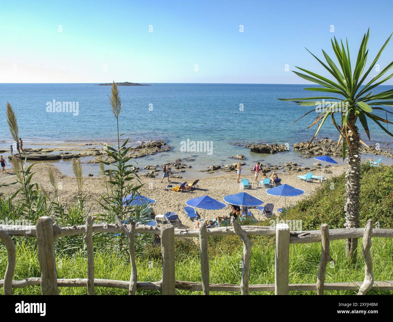 Vista della spiaggia con ombrelloni e palme, il mare largo e blu, una piccola isola in lontananza, katakolon, mediterraneo, grecia Foto Stock