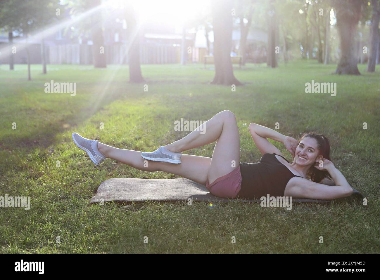 Donna che si allunga in un esercizio all'aperto sorridente felice facendo stretching dopo la corsa. Splendido modello sportivo sorridente all'aperto al tramonto d'estate Foto Stock