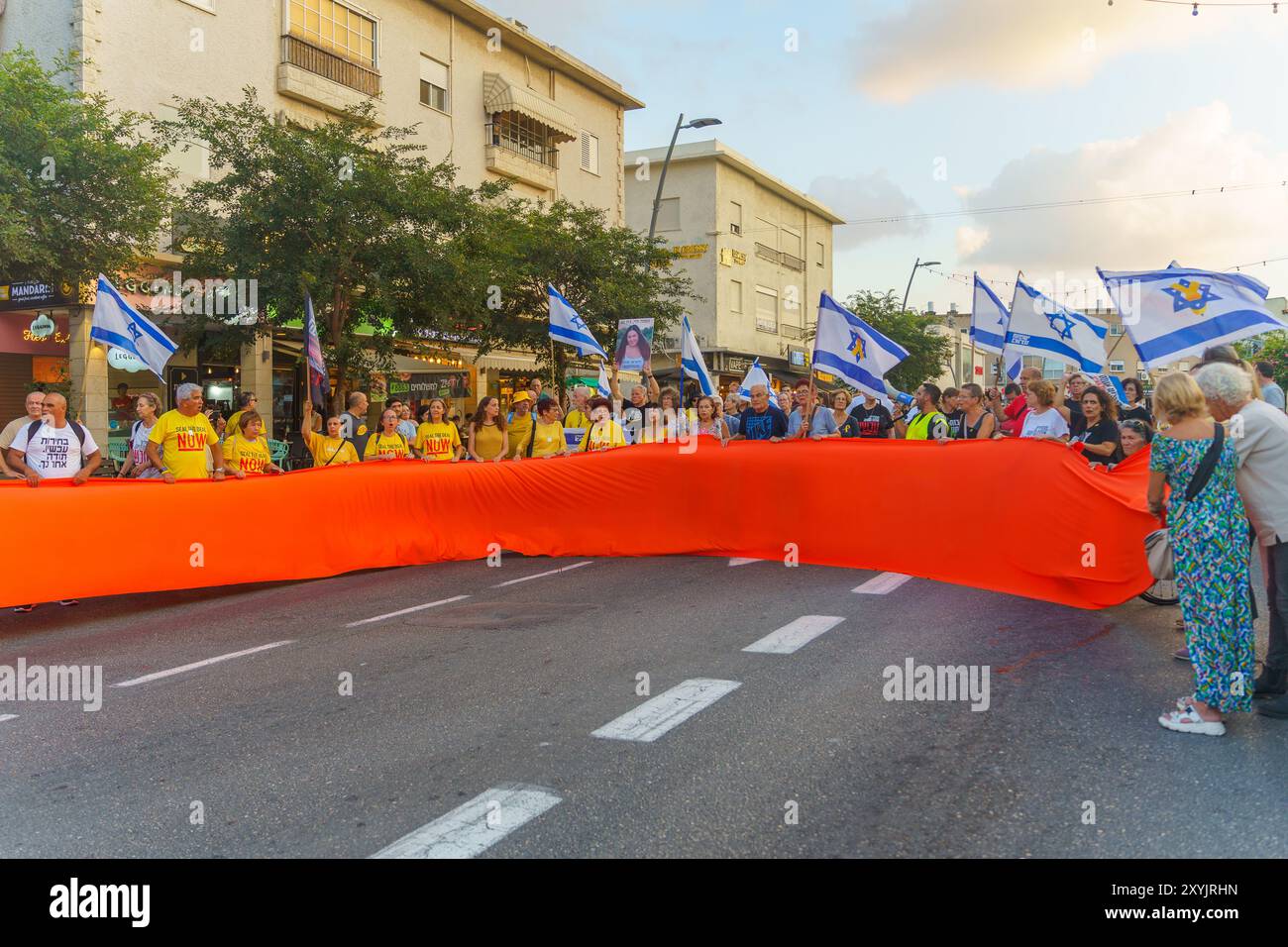 Haifa, Israele - 29 agosto 2024: Le persone stanno marciando per strada, tenendo il nastro degli ostaggi, parte di una protesta che chiede un accordo con gli ostaggi. Haifa, Israe Foto Stock