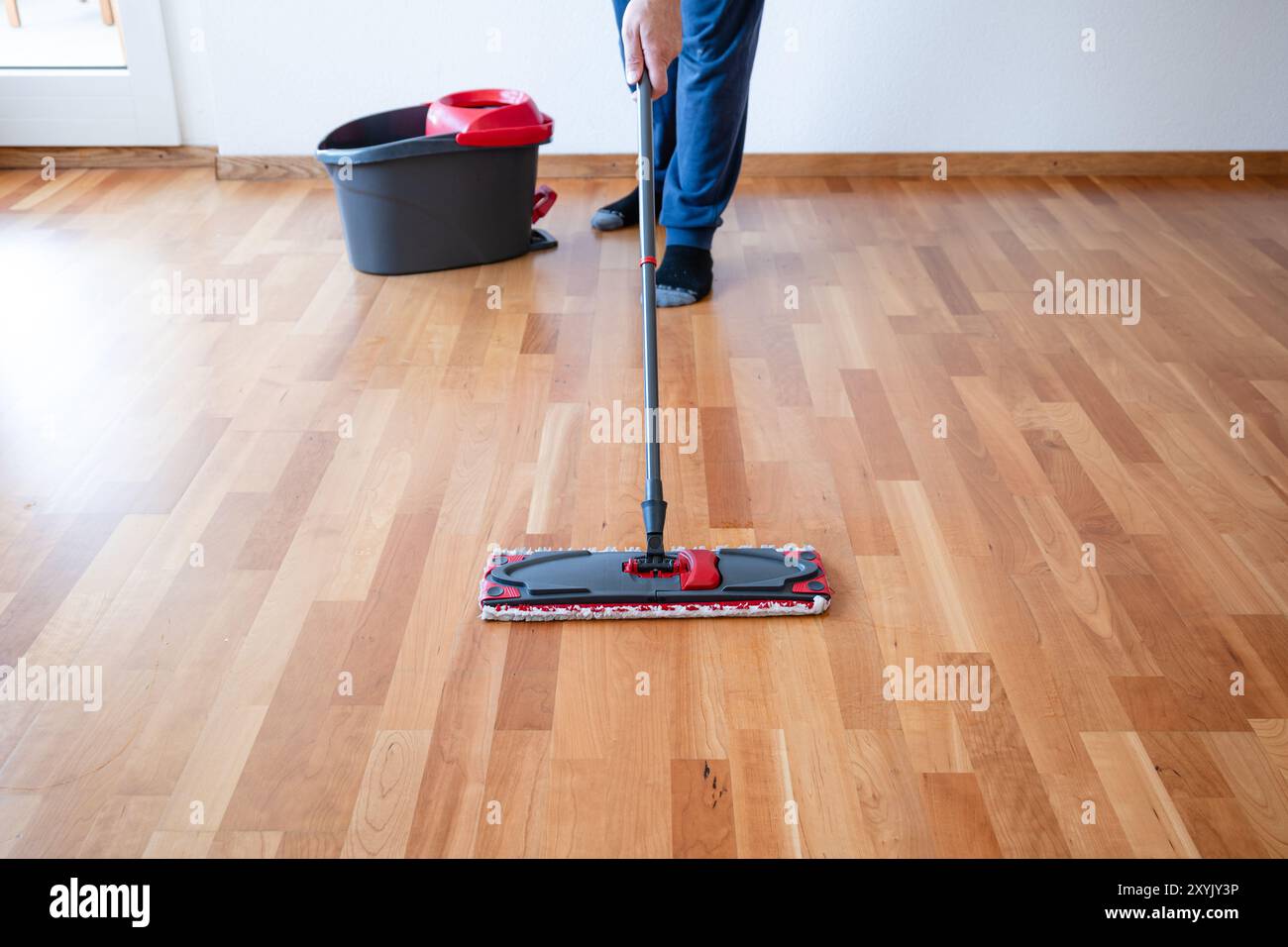 Uomo irriconoscibile che usa un mocio per la pulizia su un pavimento in piastrelle di legno dell'appartamento o pavimento in parquet. Scatto grandangolare, messa a fuoco selettiva, luminosità naturale della finestra Foto Stock