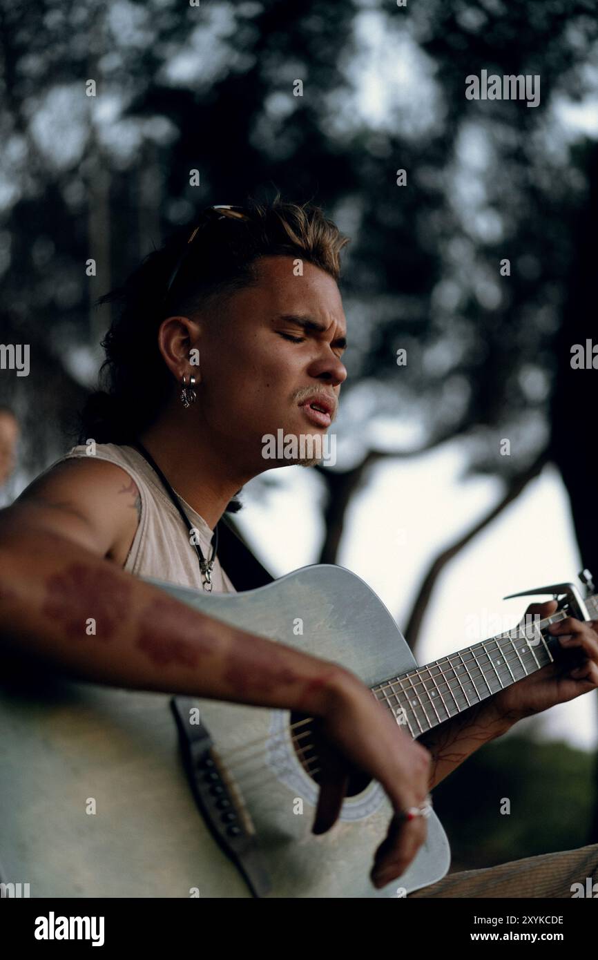 Un giovane suona una chitarra nel parco al tramonto. Foto Stock