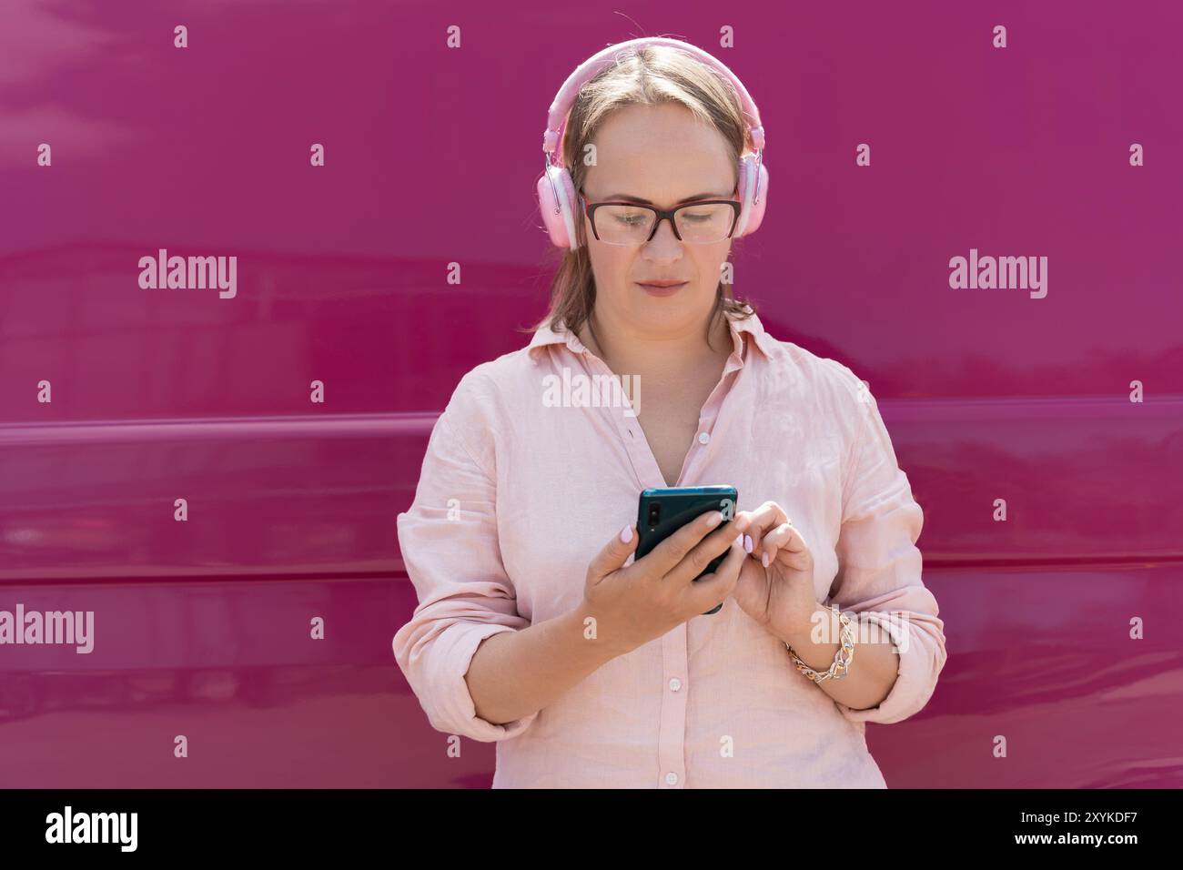 biondo su sfondo rosa brillante utilizza il telefono e ascolta la musica Foto Stock