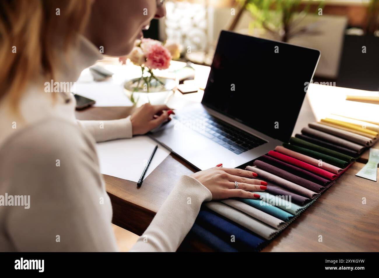 Un interior designer sta lavorando a un nuovo progetto. Scelta del colore dalla tavolozza dei colori dei tessuti per i nuovi mobili. Tavolo in legno di quercia. Tazza di caffè, fiori Foto Stock