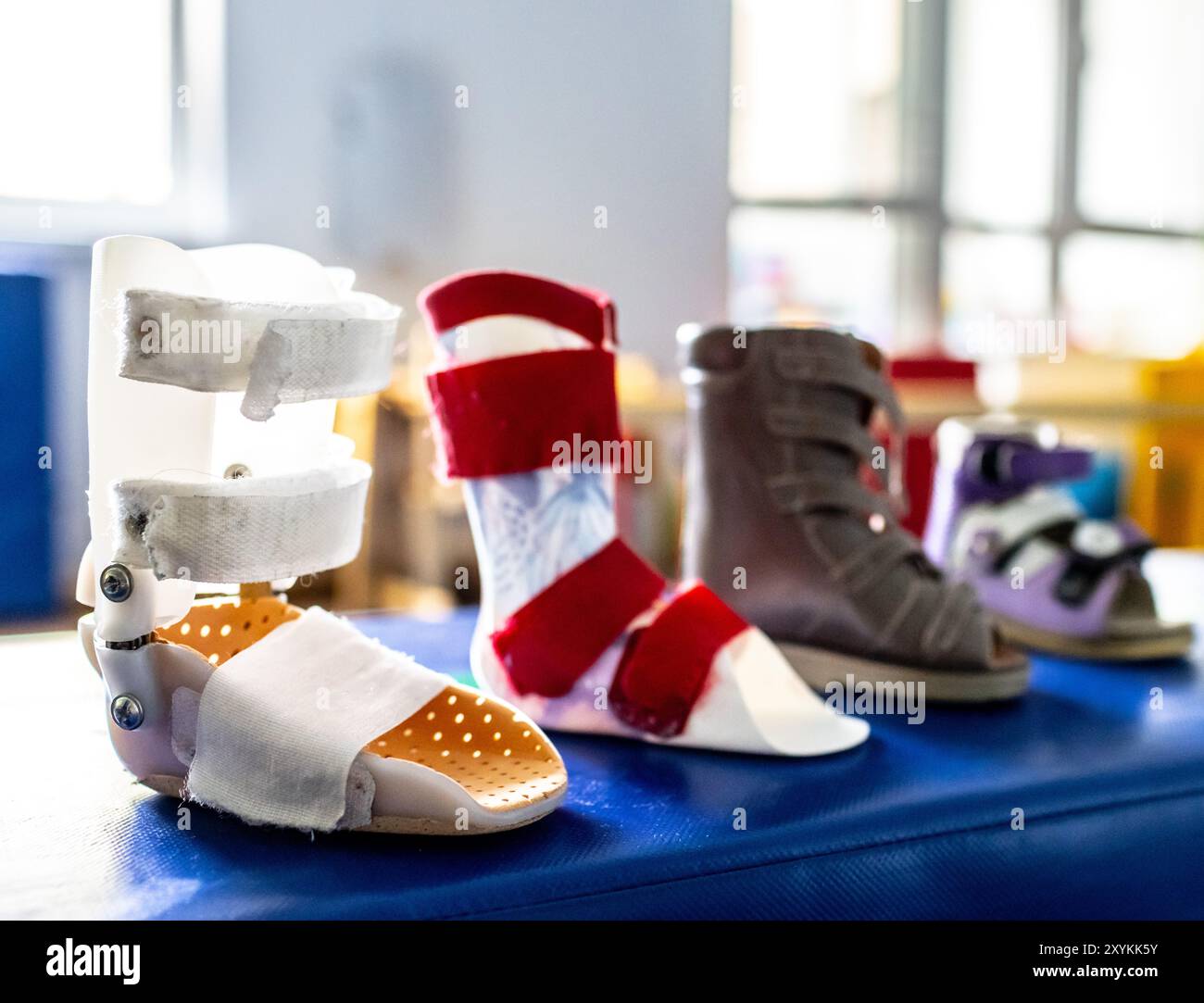 Varie scarpe riabilitative e ortosi del piede per i bambini sono esposte su un tavolo terapeutico blu in una sala ben illuminata progettata per la riabilitazione fisica Foto Stock