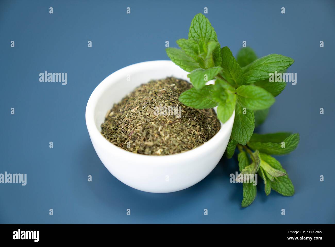 Guarnire la menta fresca su una ciotola bianca di tè alla menta essiccato, su sfondo blu. Foto Stock