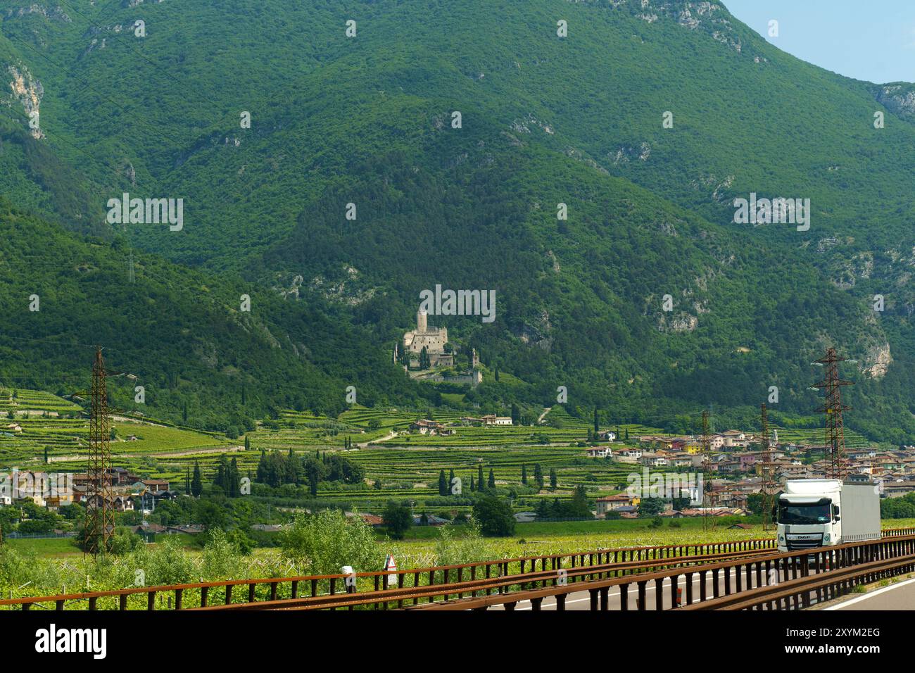 Avio, Italia - 8 giugno 2023: Un affascinante villaggio italiano con case colorate, incastonate tra verdi colline, si affaccia su un imponente castello arroccato su una collina Foto Stock