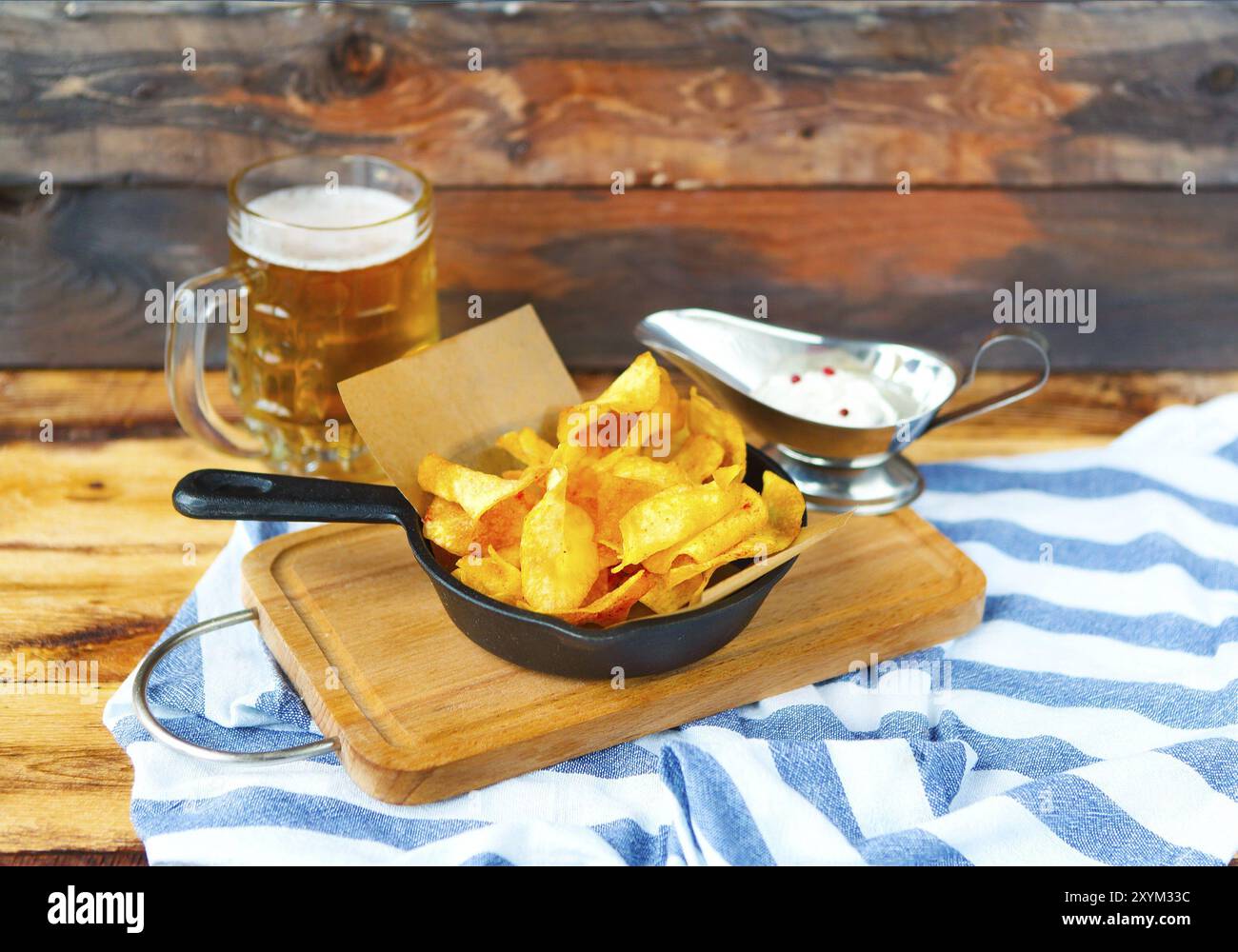 Patate fritte in padella con la salsa di aglio e una birra su di un tavolo di legno Foto Stock