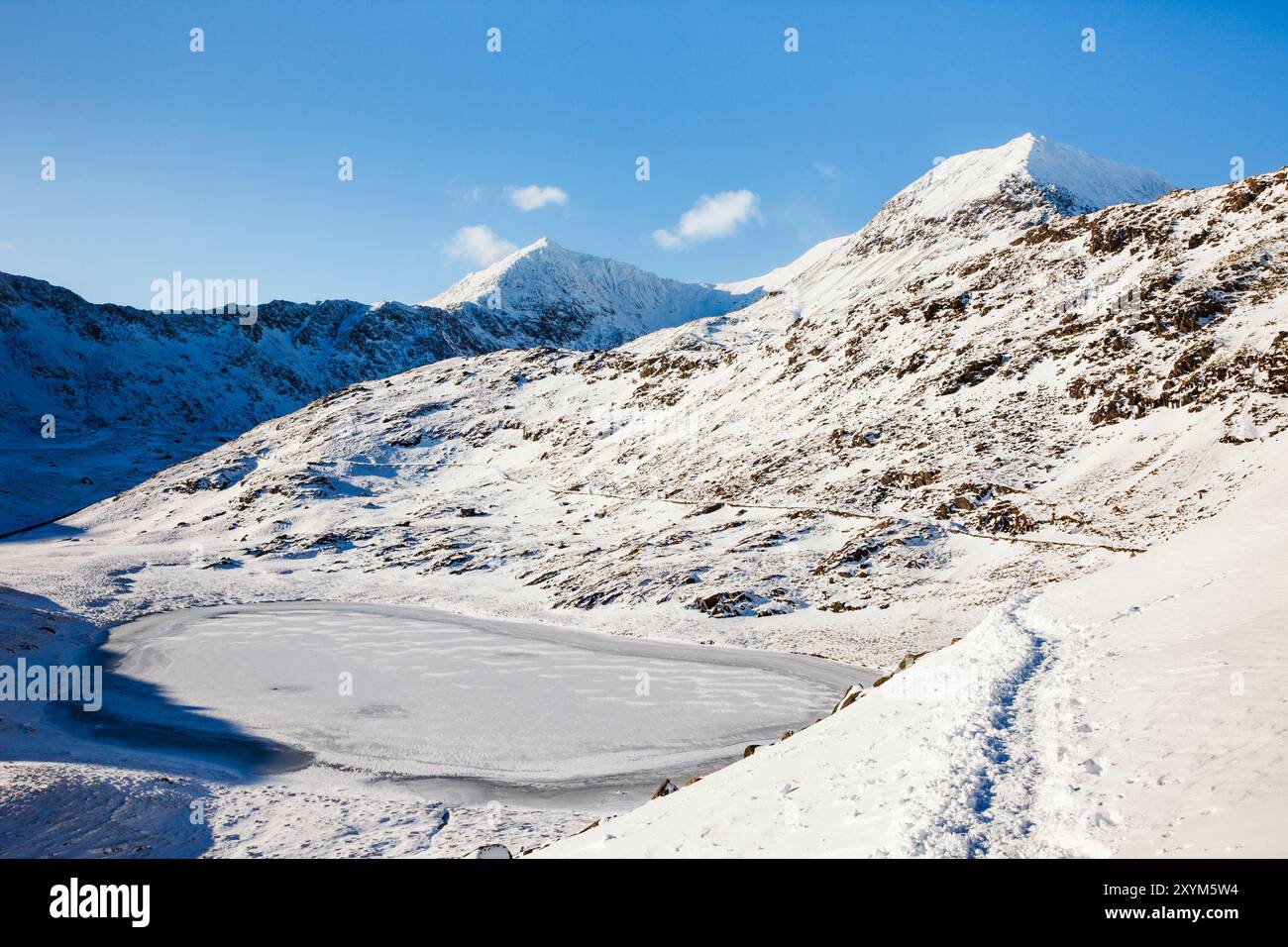 Vista del Monte Snowdon attraverso il lago ghiacciato Llyn Teyrn con neve sul Miners Track nelle montagne del Parco Nazionale di Snowdonia. Gwynedd, Galles del Nord, Regno Unito Foto Stock
