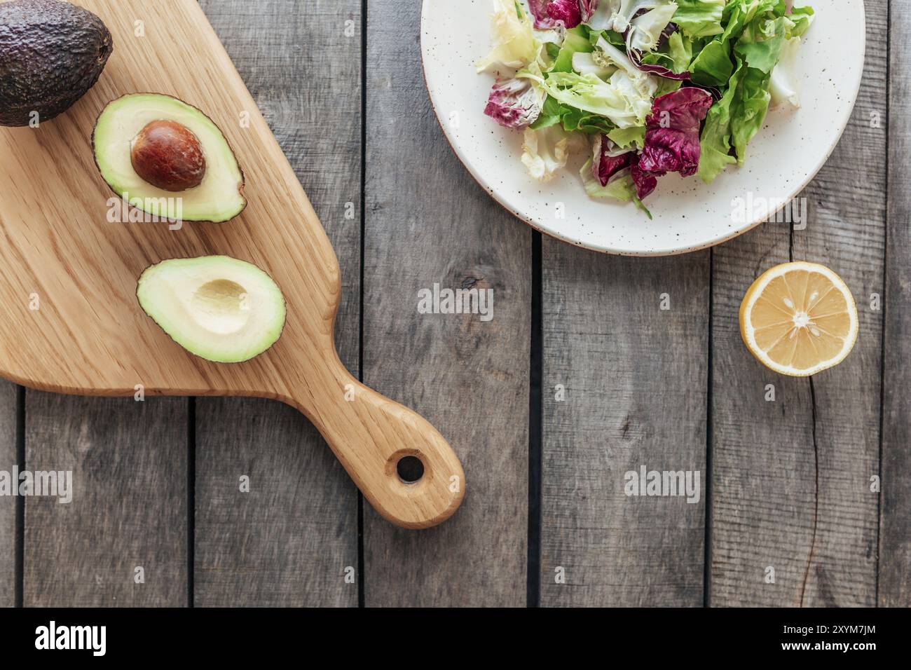 Concetto sano di mangiare piatto posato. Dieta mediterranea, piatto con foglie fresche di insalata di lattuga verde, foglie di radicchio viola, tagliere con avocado Foto Stock