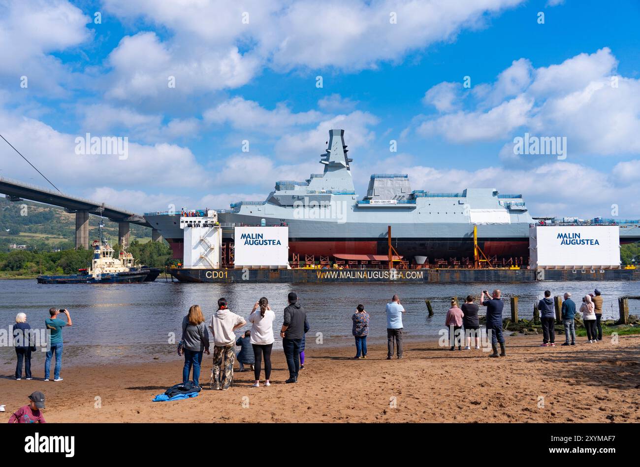Erskine, Scozia, Regno Unito. 30 agosto 2024. La fregata HMS Cardiff Type 26 fu lanciata sulla chiatta presso il cantiere BAE Systems di Govan, Glasgow. La nave da guerra viene trasportata su chiatta a Glenmallan sul Loch Long, dove verrà scaricata dalla chiatta. Successivamente sarà rimorchiata al cantiere BAE di Yoker per l'allestimento adiacente alla nave gemella HMS Glasgow. PIC; HMS Cardiff presso il ponte Erskine osservata da membri del pubblico. Iain Masterton/Alamy Live News Foto Stock
