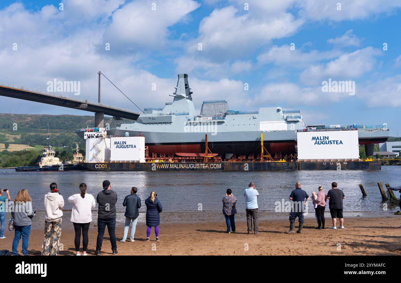 Erskine, Scozia, Regno Unito. 30 agosto 2024. La fregata HMS Cardiff Type 26 fu lanciata sulla chiatta presso il cantiere BAE Systems di Govan, Glasgow. La nave da guerra viene trasportata su chiatta a Glenmallan sul Loch Long, dove verrà scaricata dalla chiatta. Successivamente sarà rimorchiata al cantiere BAE di Yoker per l'allestimento adiacente alla nave gemella HMS Glasgow. PIC; HMS Cardiff presso il ponte Erskine osservata da membri del pubblico. Iain Masterton/Alamy Live News Foto Stock