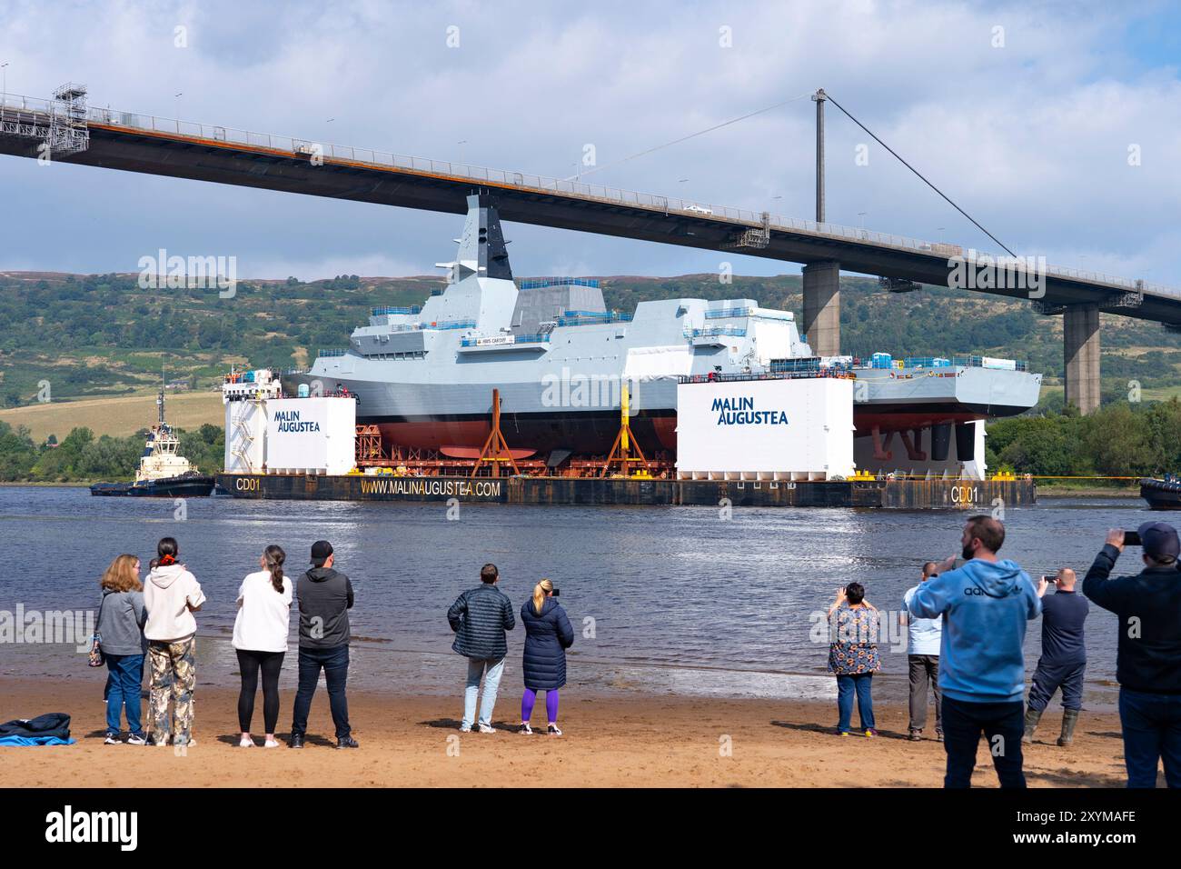Erskine, Scozia, Regno Unito. 30 agosto 2024. La fregata HMS Cardiff Type 26 fu lanciata sulla chiatta presso il cantiere BAE Systems di Govan, Glasgow. La nave da guerra viene trasportata su chiatta a Glenmallan sul Loch Long, dove verrà scaricata dalla chiatta. Successivamente sarà rimorchiata al cantiere BAE di Yoker per l'allestimento adiacente alla nave gemella HMS Glasgow. PIC; HMS Cardiff presso il ponte Erskine osservata da membri del pubblico. Iain Masterton/Alamy Live News Foto Stock
