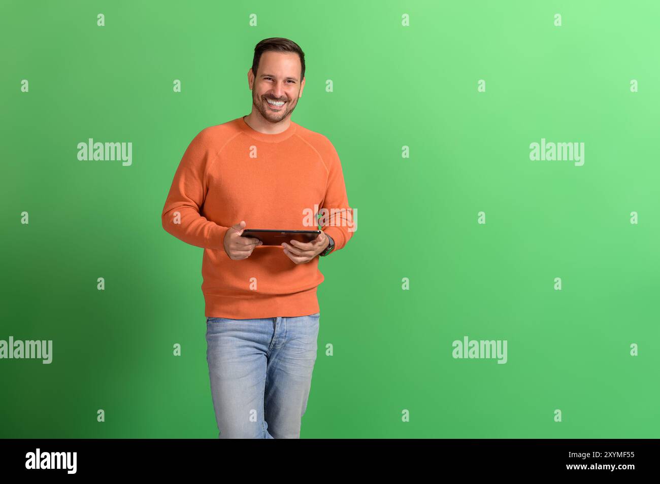 Ritratto di un bellissimo professionista sorridente che controlla le e-mail su un tablet digitale su sfondo verde Foto Stock