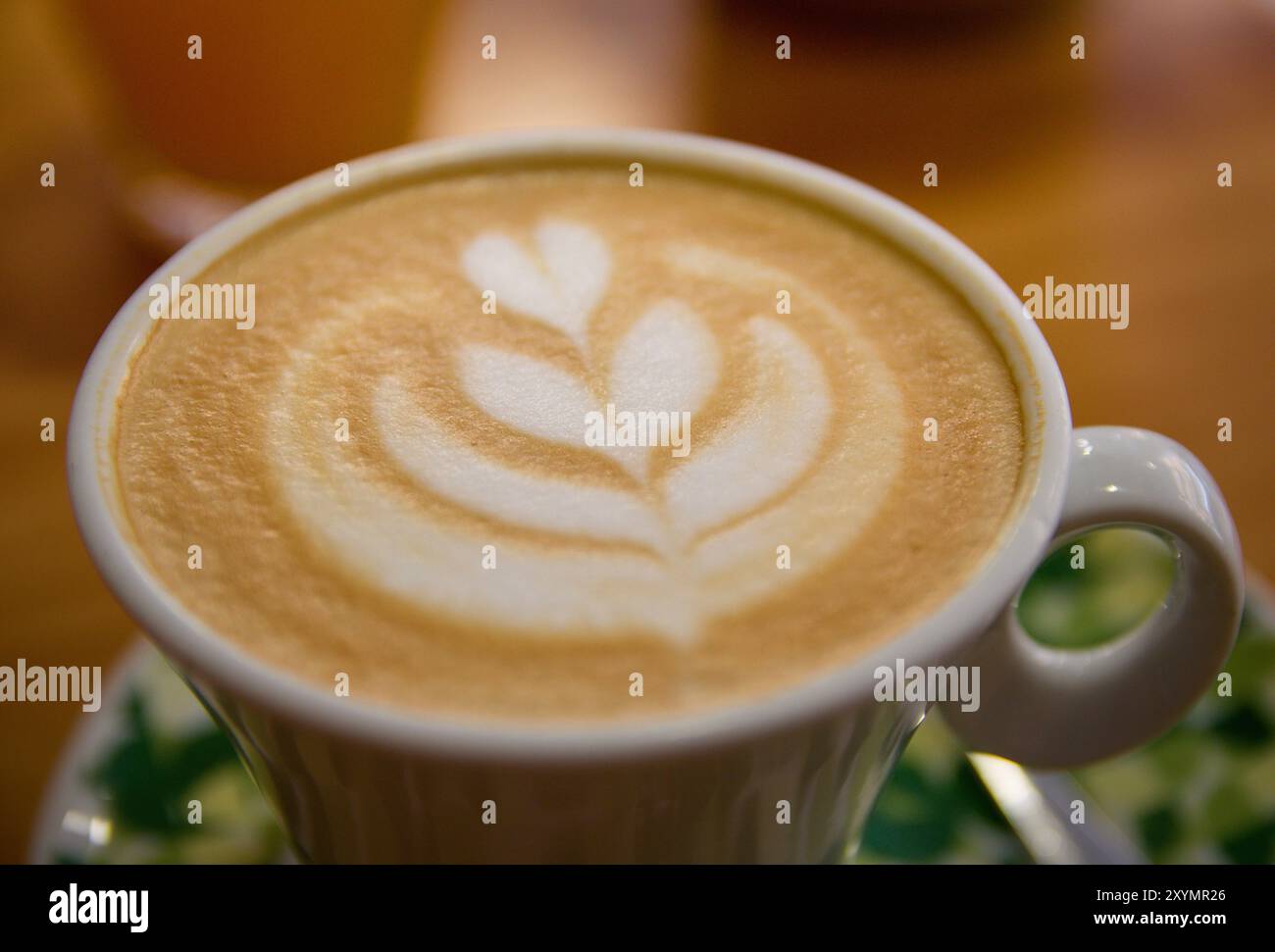 Primo piano di un fiore disegnato utilizzando tecniche di latte art su una tazza di caffè latte durante la colazione in un bar Foto Stock