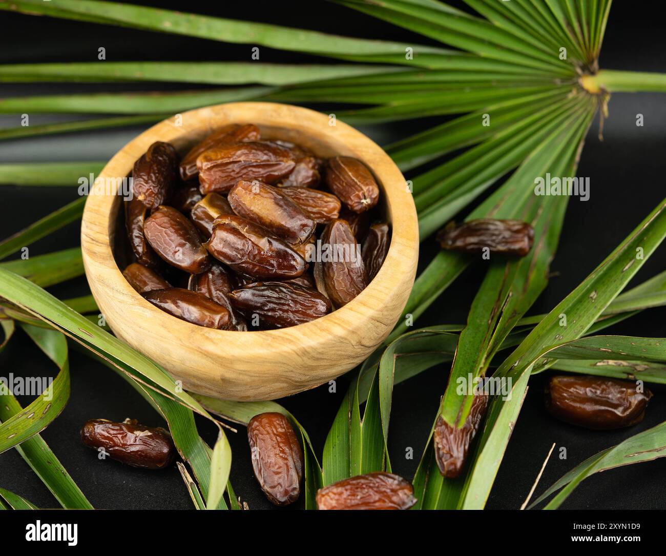 Datteri in una ciotola di legno su una foglia di palma Foto Stock