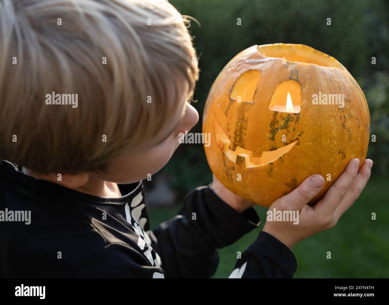 il bambino tiene tra le mani ed esamina una zucca arancione con una candela amara all'interno. Preparatevi per Halloween. Non aver paura, divertiti Foto Stock