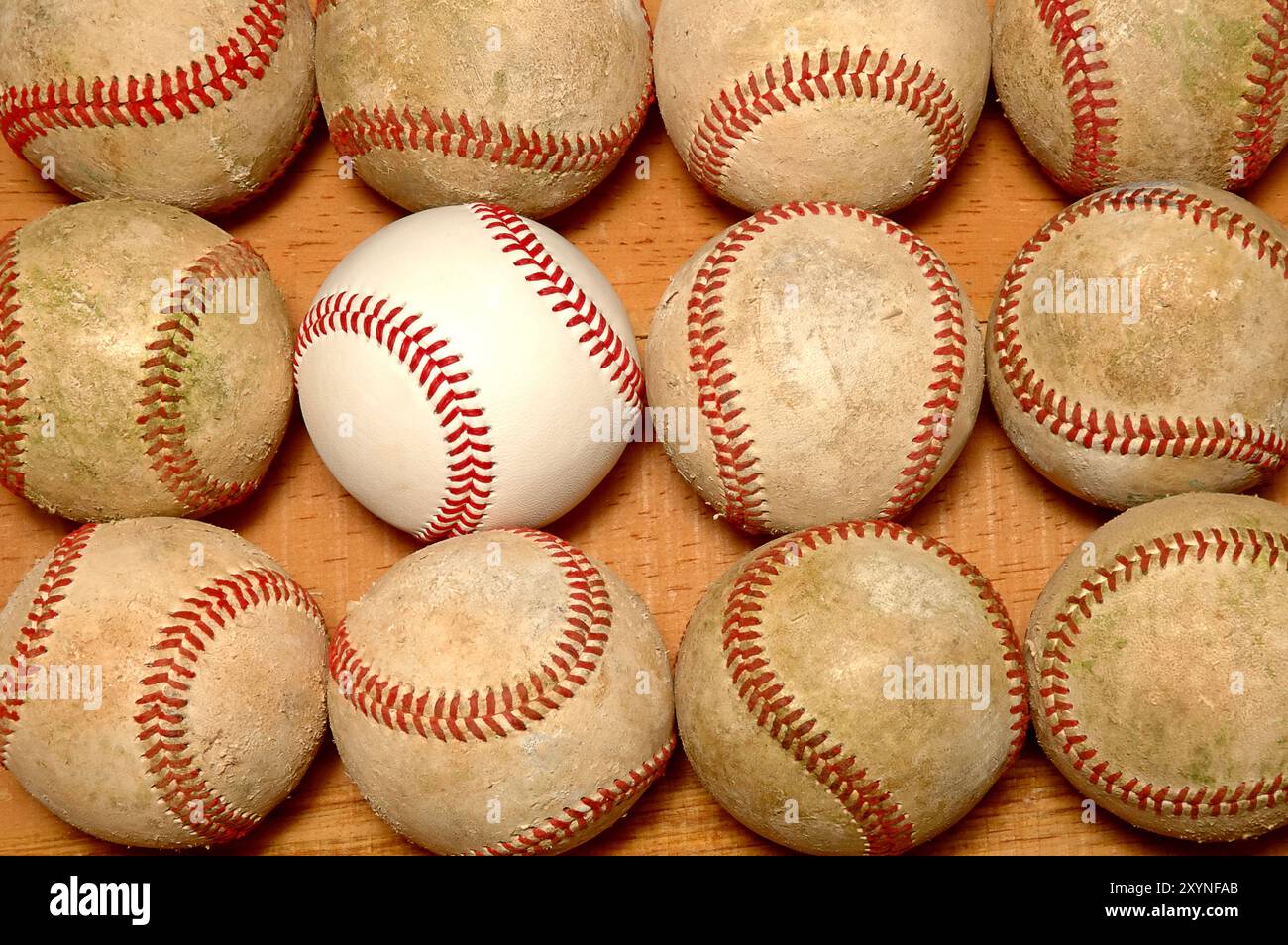 Posa piatta di una dozzina di palle di base su una superficie di legno, una nuova palla viene inserita tra le vecchie palle usate. Foto Stock