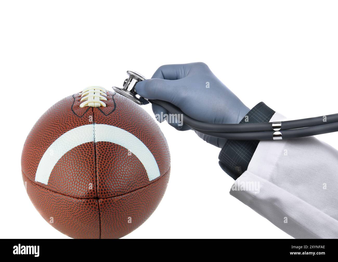 Concetto di commozione calcistica: Primo piano di un football americano con una mano del medico che tiene uno stetoscopio contro la palla, isolato sul bianco. Foto Stock